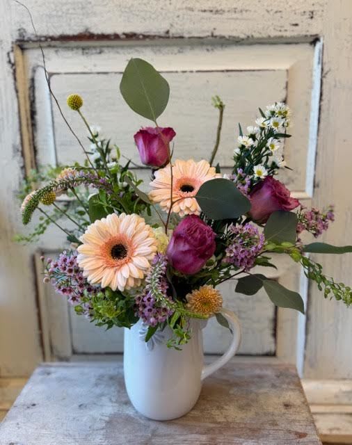 Modern Farmhouse Pitcher - A charming arrangement of seasonal flowers, fillers and foliage in a ceramic pitcher that is 8" tall. Flower varieties will vary based on inventory. The pitcher comes either white or pink- if you have a preference please specify in the notes section of your order.