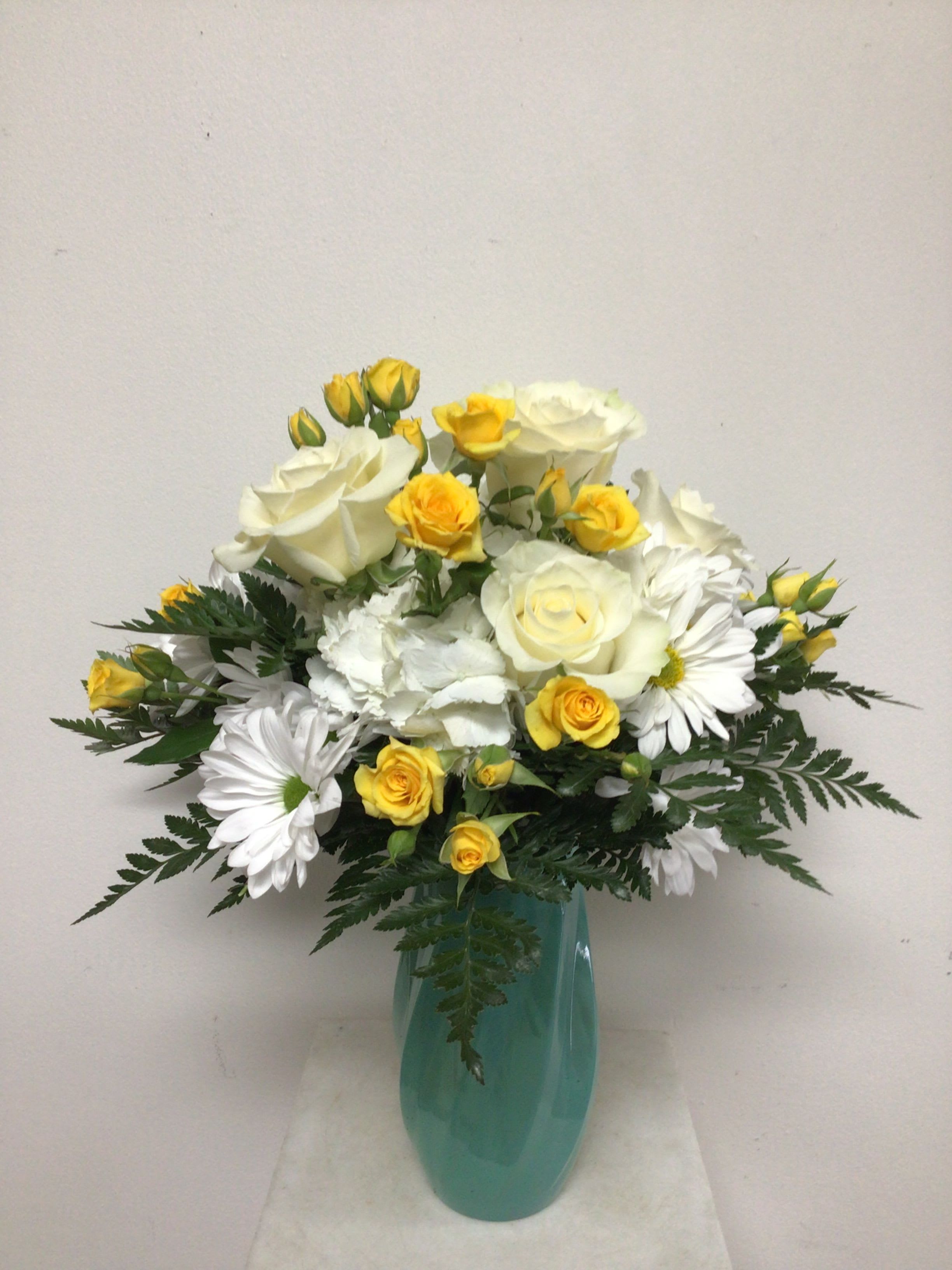 Summer Fun - 8 inch tall turquoise swirl vase is arranged with white daisies, white hydrangea, cream roses, yellow spray roses and mixed greenery. Approximate size is 18 inches tall by 13 inches wide.