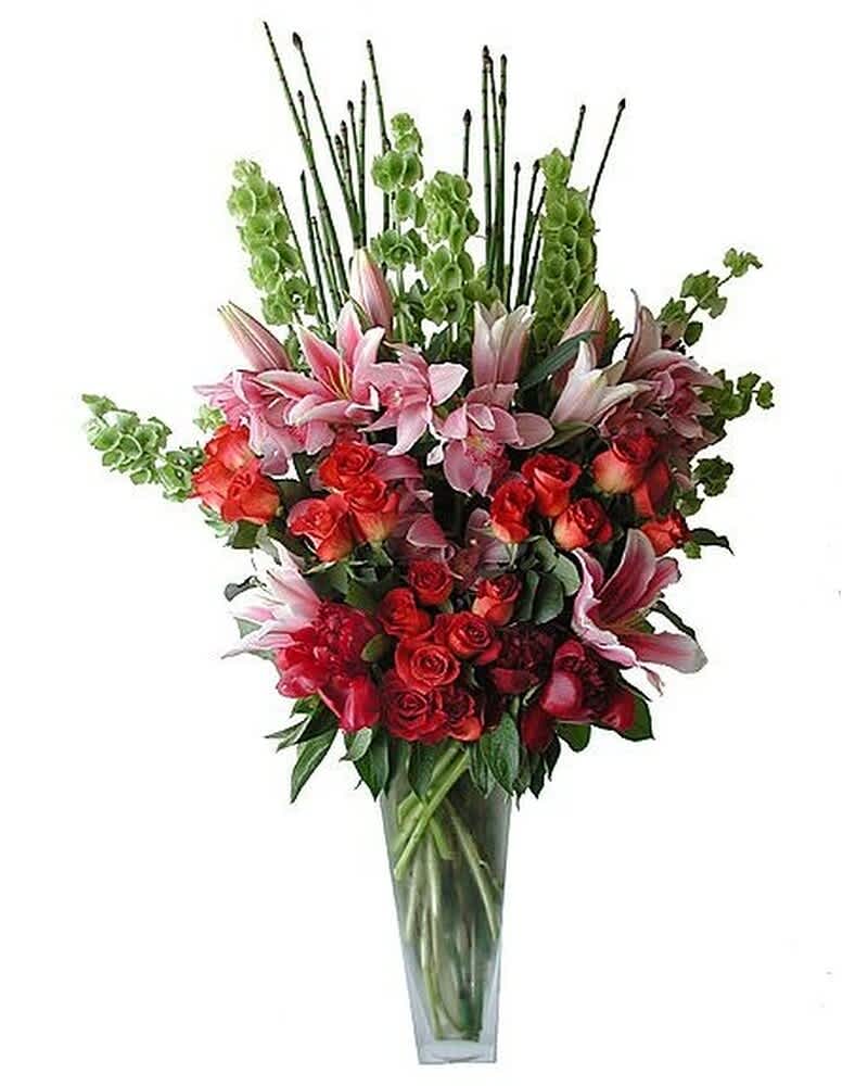 Tall arrangement of pink lilies, red roses, and green bells of Ireland in a clear glass vase.