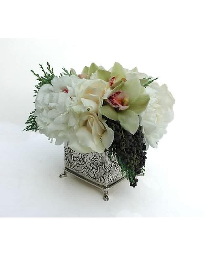Low white and green floral arrangement with orchids in an ornate silver cube vase