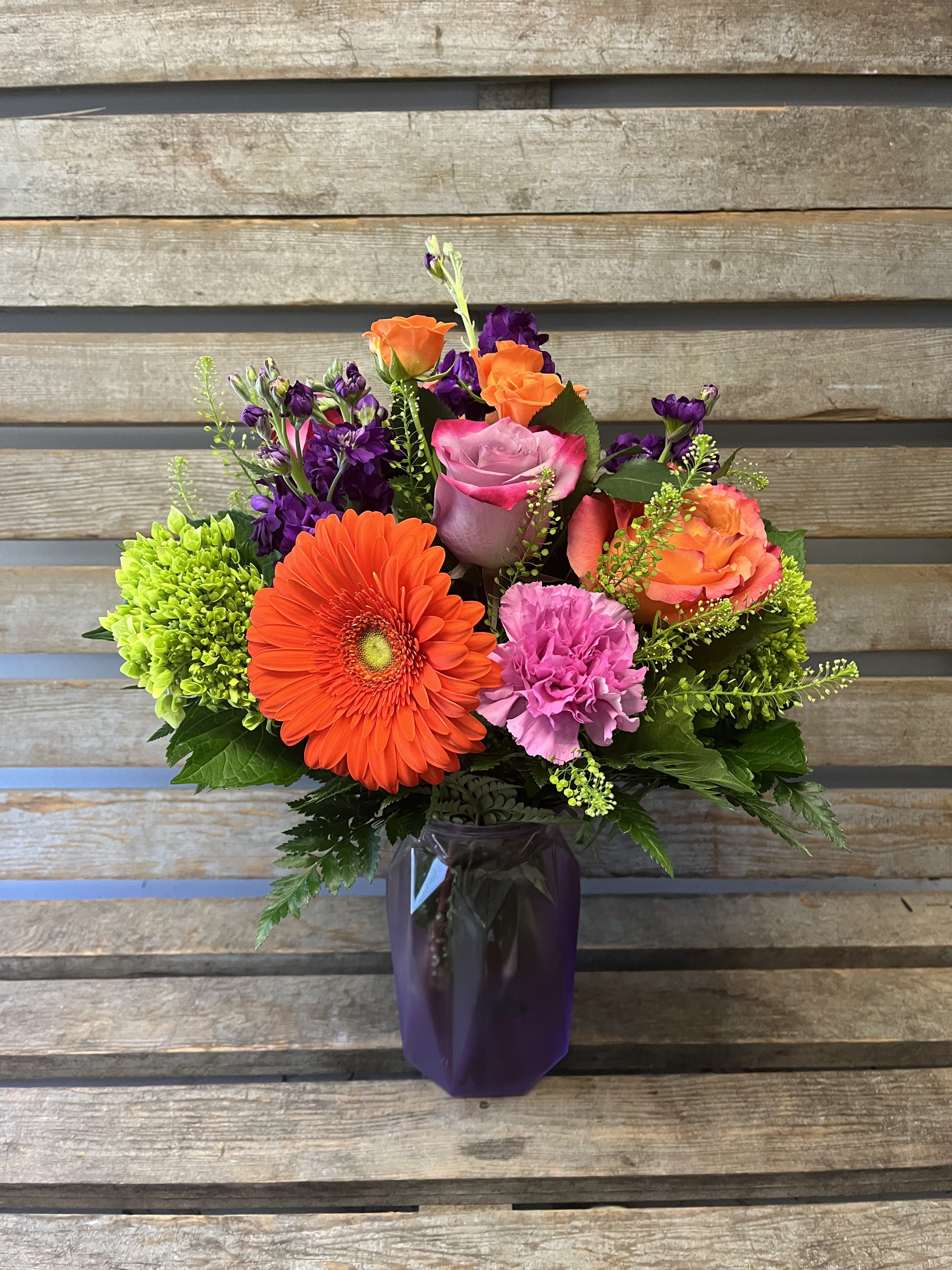 Mother’s Day, purple and orange Sofia vase  - Purple frosted Sofia vase filled with fresh flowers and shades of purples and oranges. Designers’s choice.Designers choice of flowers keeping with the color scheme and the Mother’s Day holiday.