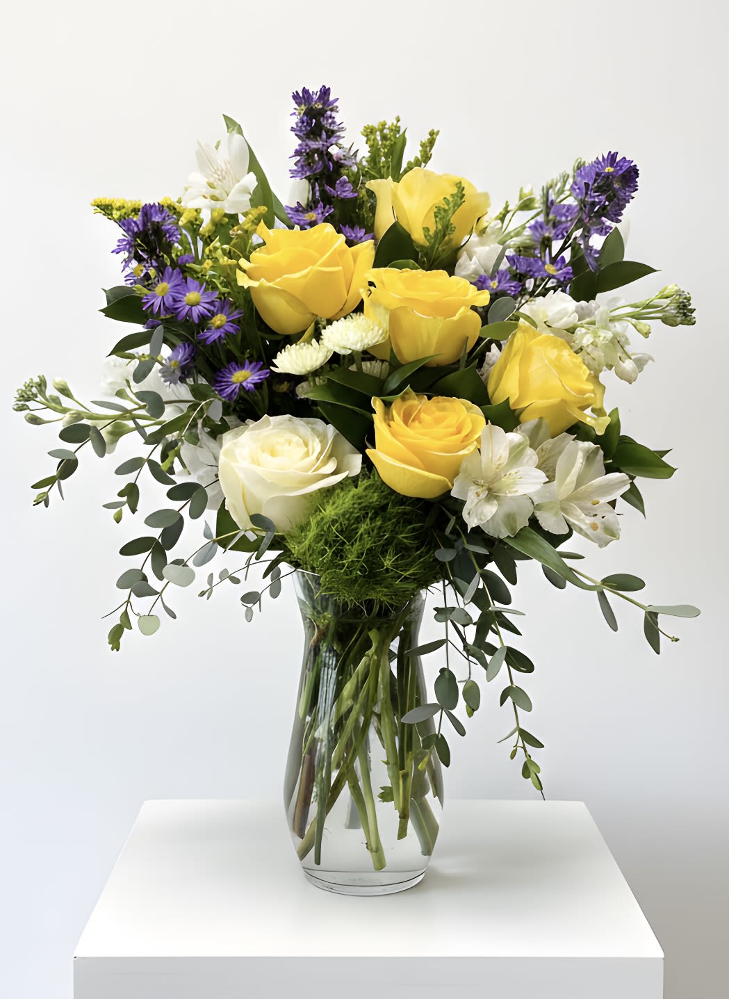 Mixed bouquet of yellow and white roses with purple flowers in a clear glass vase