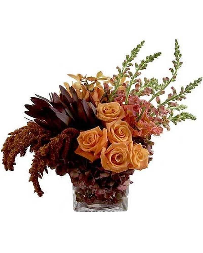 Low arrangement of orange roses, dark protea, and pink snapdragons in a square glass vase