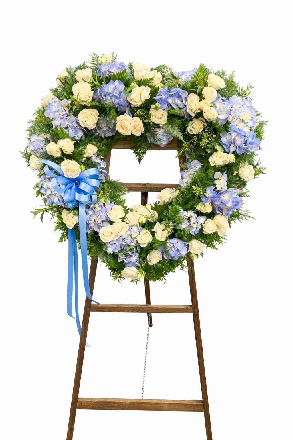 Forever In Our Hearts - This graceful sympathy heart easel is designed in soothing shades of soft blue and ivory to honor a cherished life with beauty and peace. Light blue hydrangeas, creamy white roses, and lush evergreen accents are arranged in an open heart shape and finished with a coordinating blue ribbon for a timeless tribute.  Perfect for funeral services, memorials, or graveside ceremonies, this standing heart offers a heartfelt expression of love, remembrance, and sympathy.  Flower varieties and shades may vary slightly based on seasonal availability, while maintaining the overall style, color palette, and value of the arrangement.
