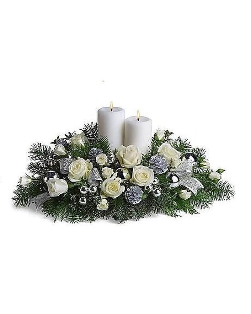 Low centerpiece of white roses and evergreens with two white pillar candles and silver decorations