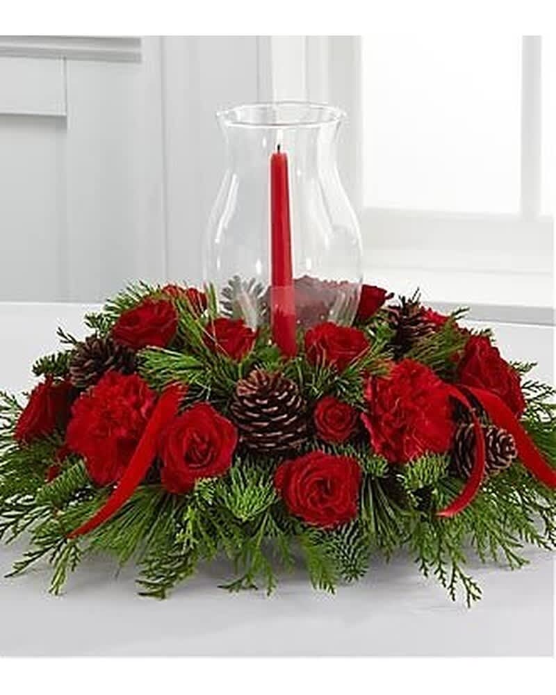 Low centerpiece of red roses and carnations with pinecones around a red candle in a glass hurricane.