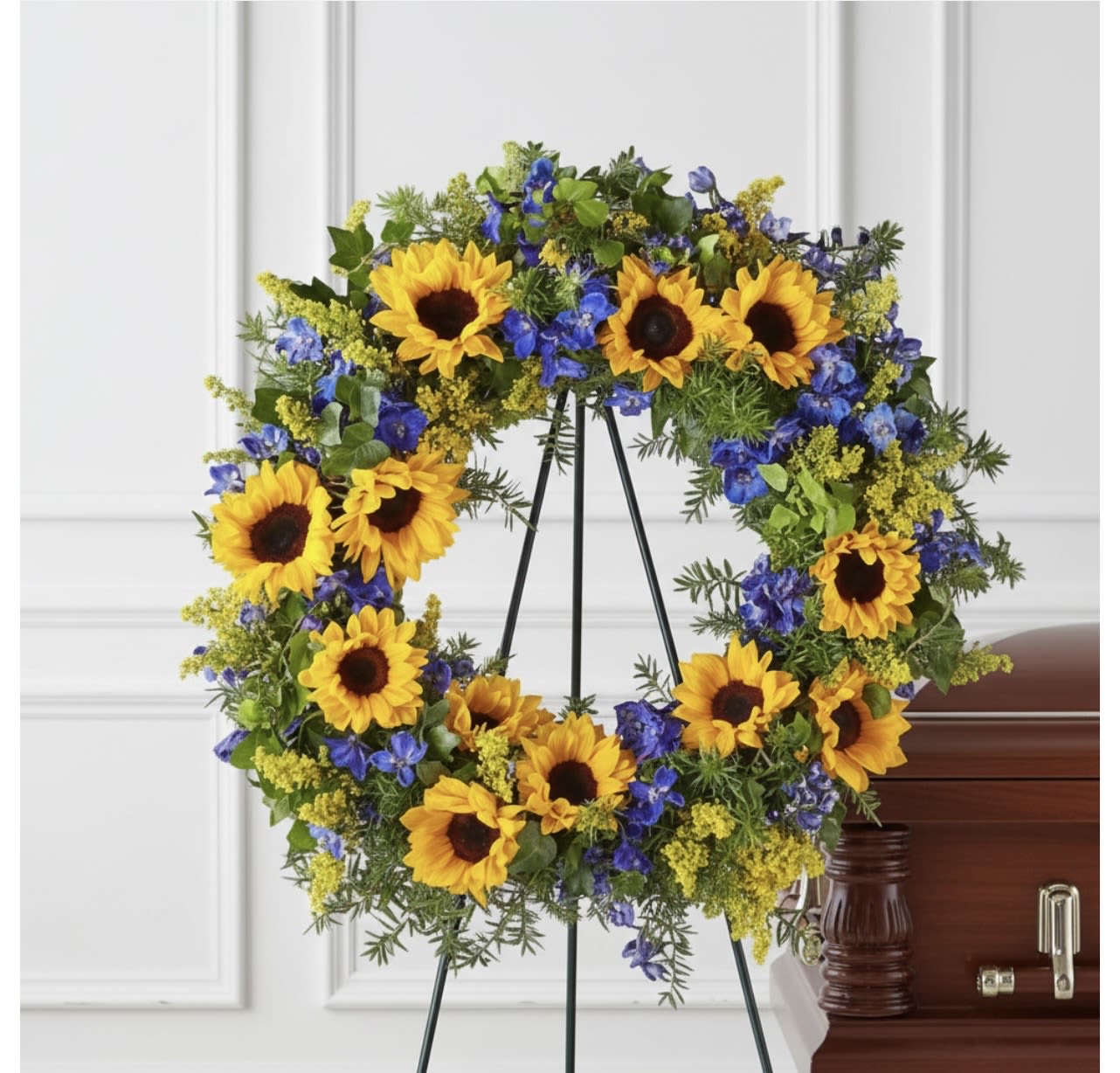 Sunflower and blue flower wreath on a standing easel beside a casket