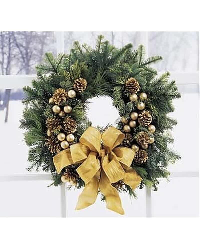 Evergreen wreath with gold pine cones, ornaments, and a large gold bow hanging on a window