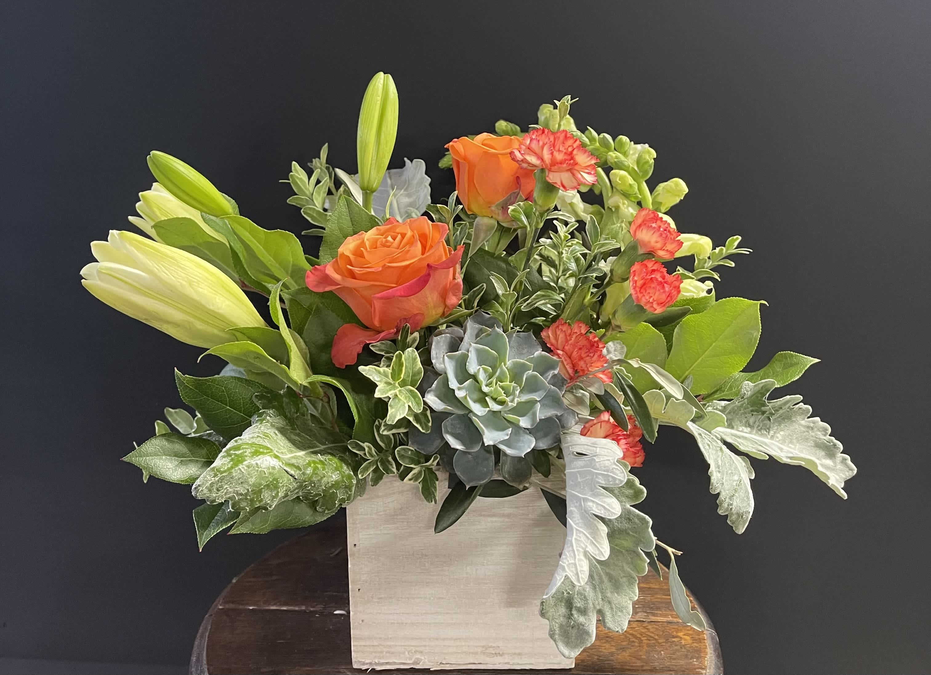 Orange roses and lilies in a square wooden container with succulents