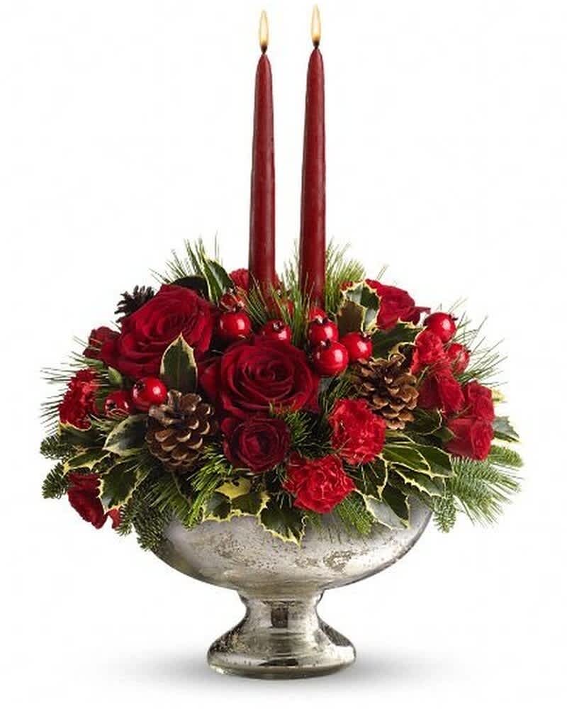 Low red rose and carnation centerpiece with holly, pinecones, and two tall red taper candles in a silver bowl.