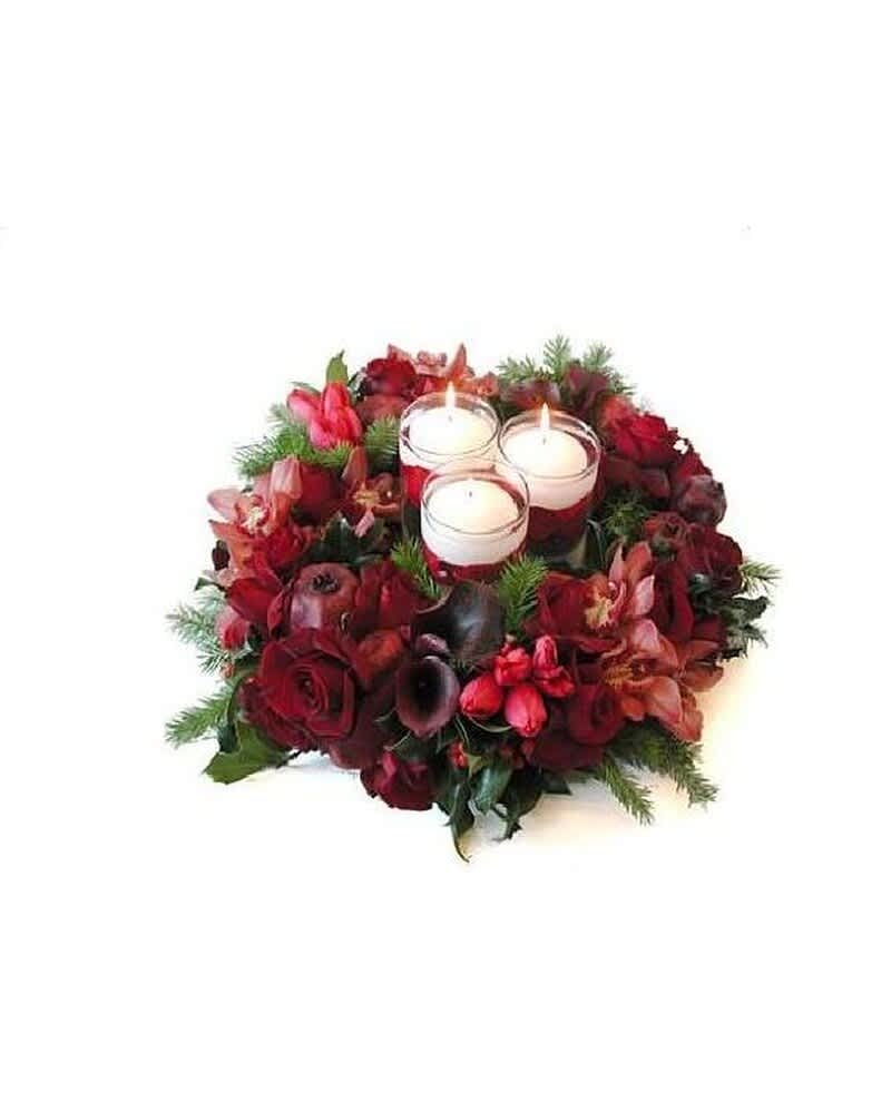 Round arrangement of dark red flowers with three white votive candles in glass at the center