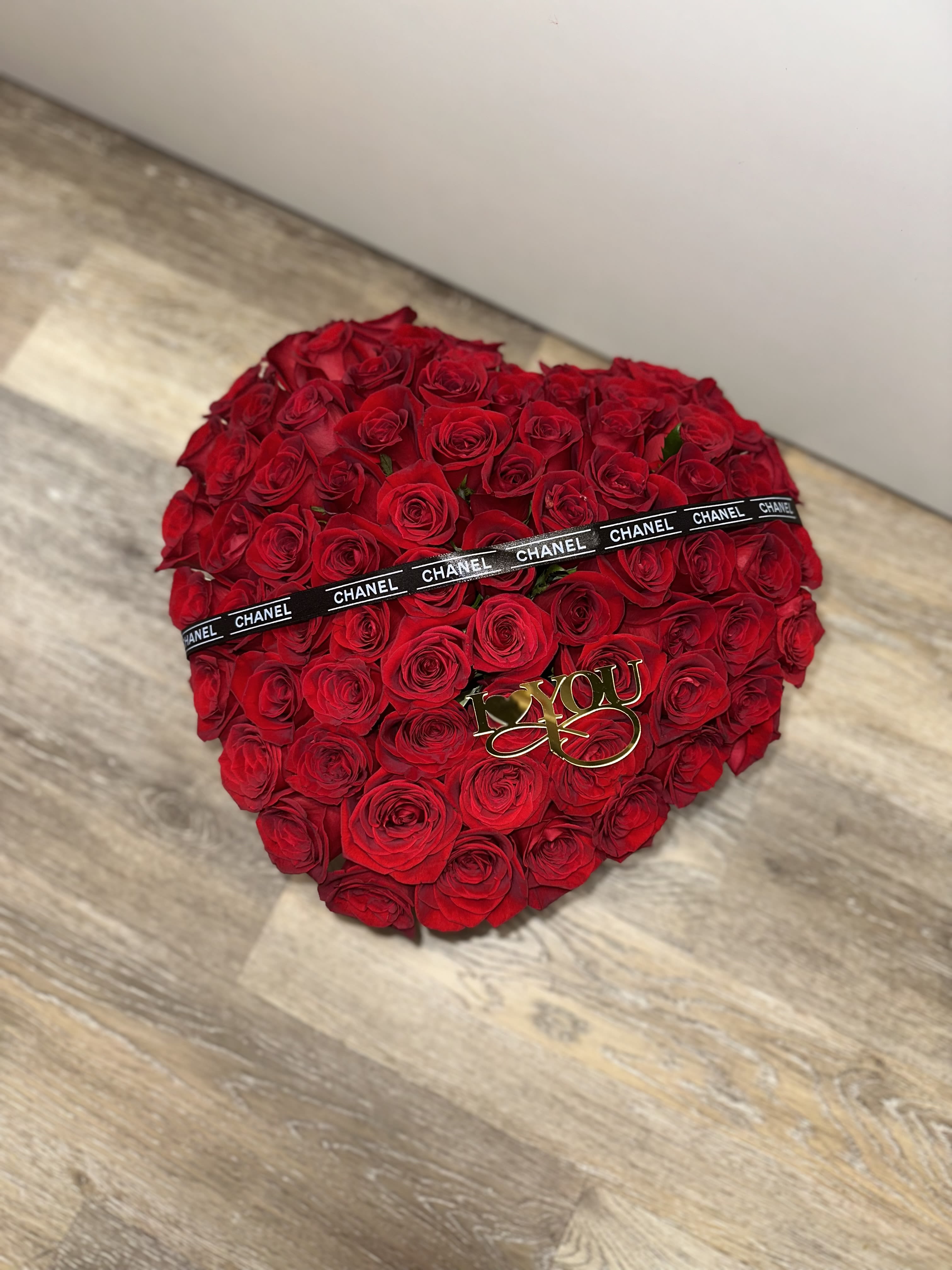 Heart-shaped bouquet of red roses with a black ribbon and gold "I love you" topper
