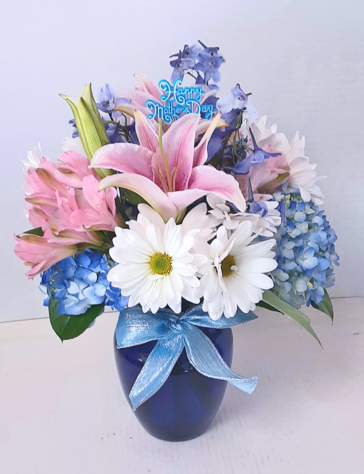 Love You Mom! - A beautiful arrangement of blue hydrangea, delphinium, assorted alstromeria, and pink lilies in a cobalt blue vase. Add a Mothers day mylar balloon for just the right Mothers' Day touch!