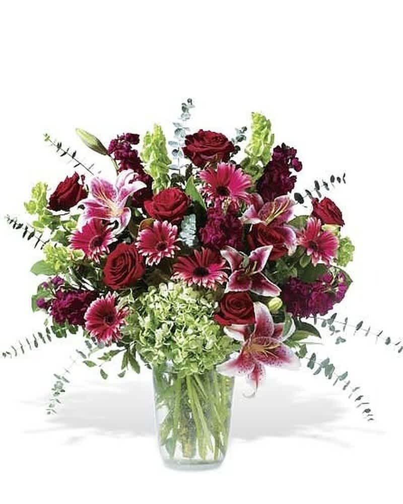 Tall arrangement of red roses, pink lilies, gerbera daisies, and green hydrangea in a clear glass vase