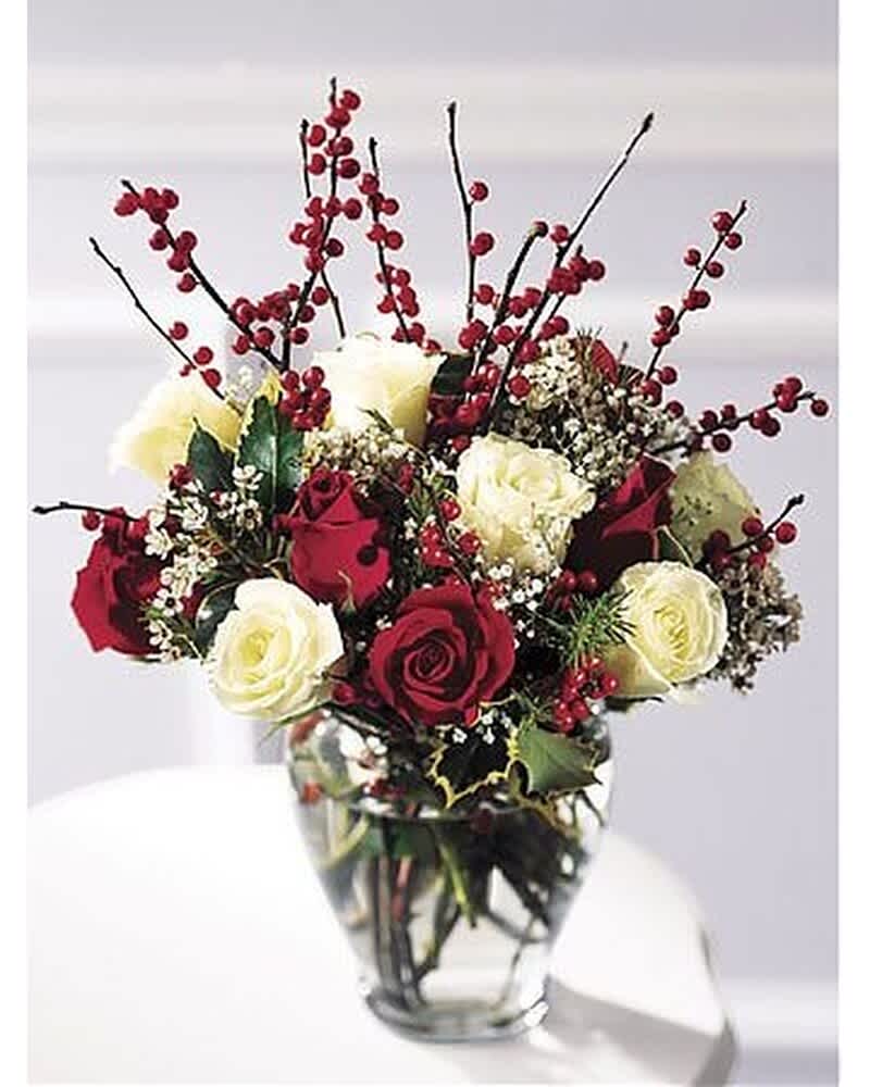 Arrangement of red and white roses with red berries and filler flowers in a clear glass vase