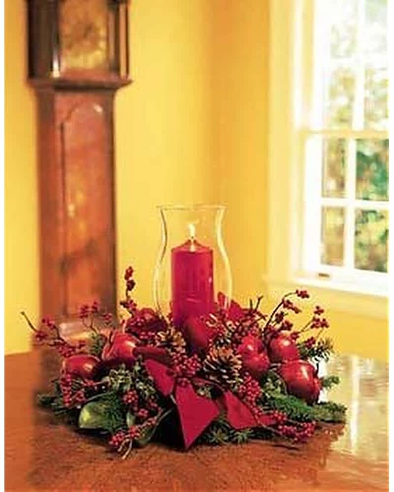 Red candle centerpiece with berries, apples, and pinecones on a table