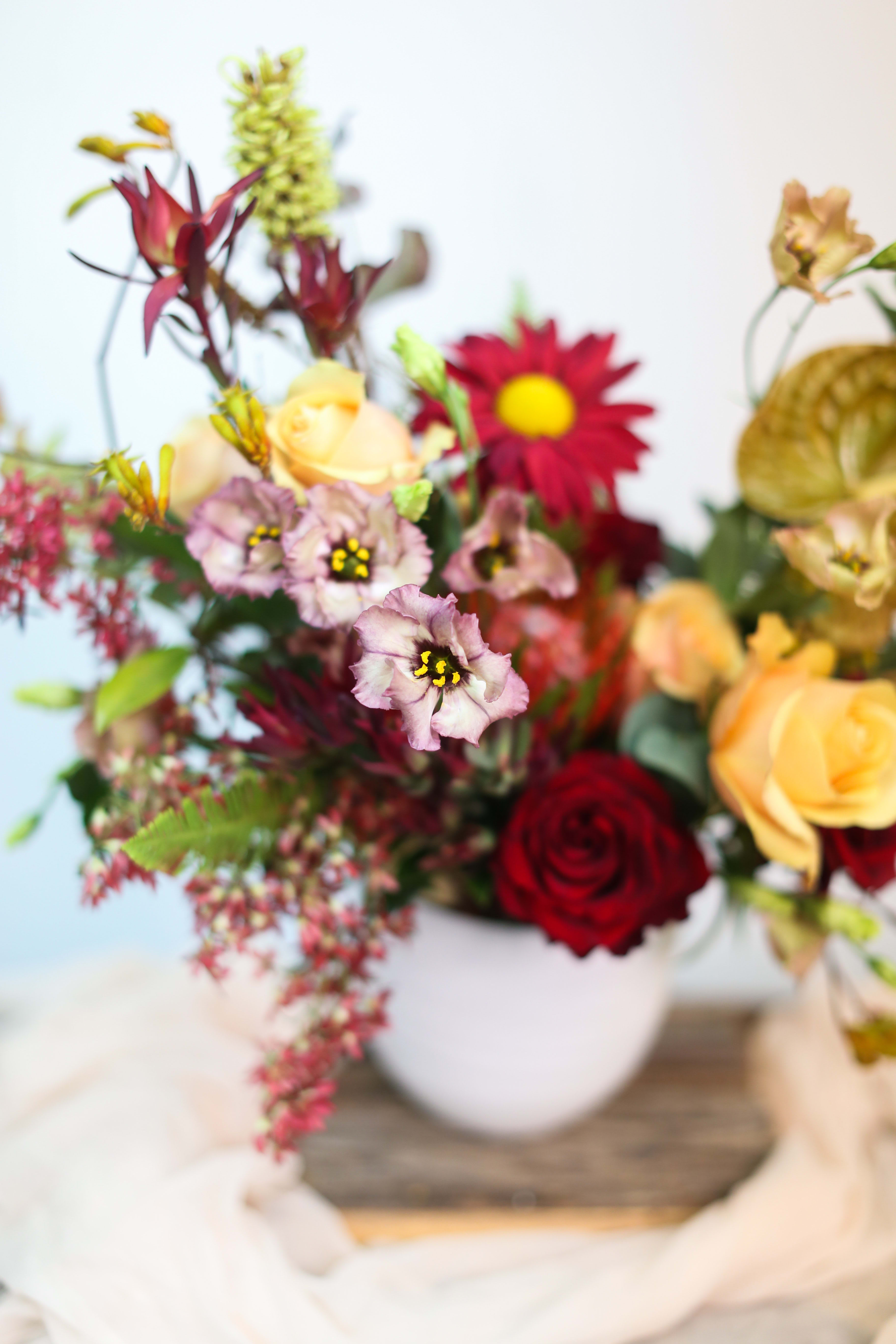 Mixed bouquet with roses and daisy-like blooms in a white vase