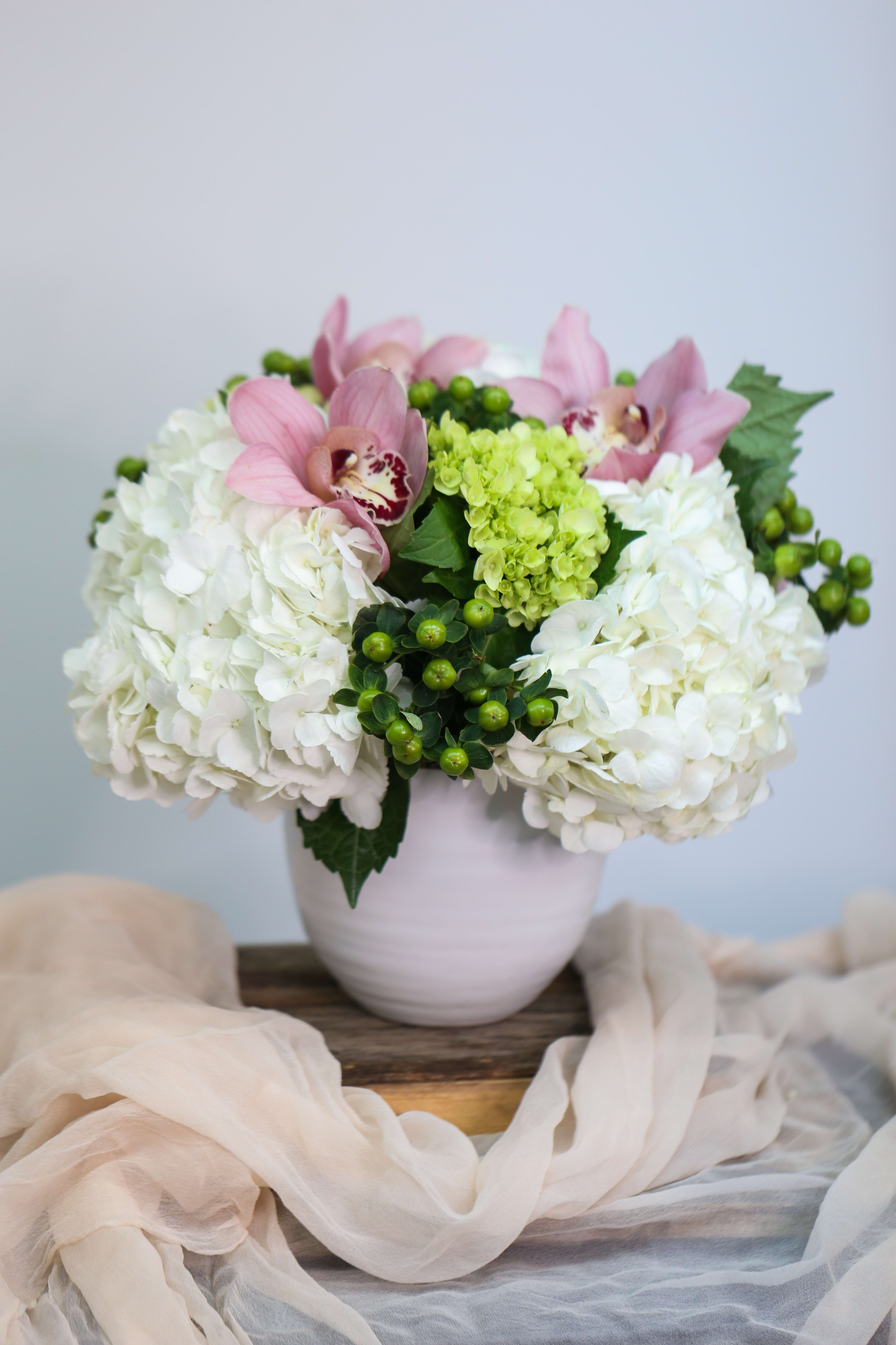 Pink orchids and white hydrangeas arranged in a pale vase