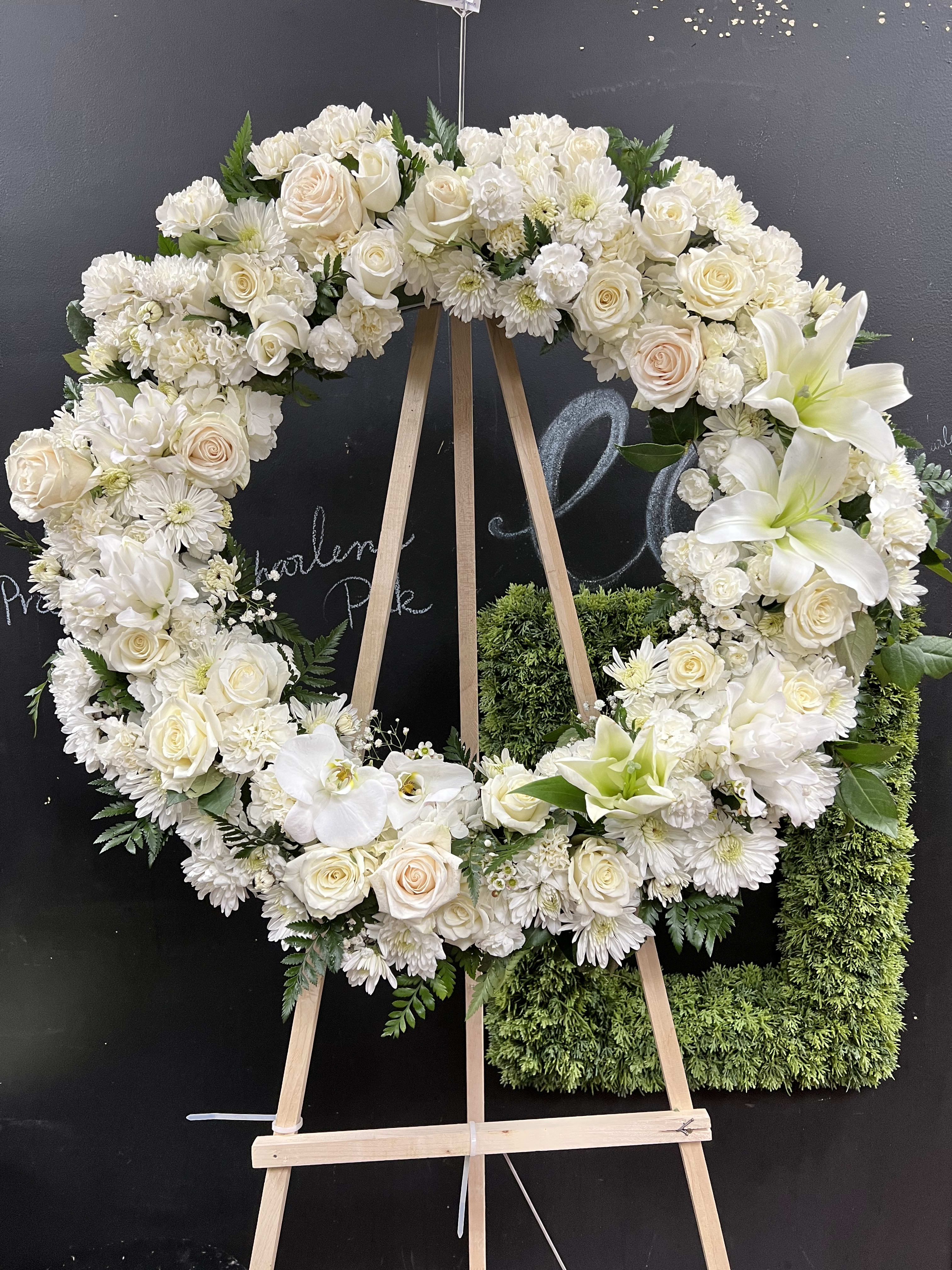 White floral wreath on a wooden easel with roses and lilies