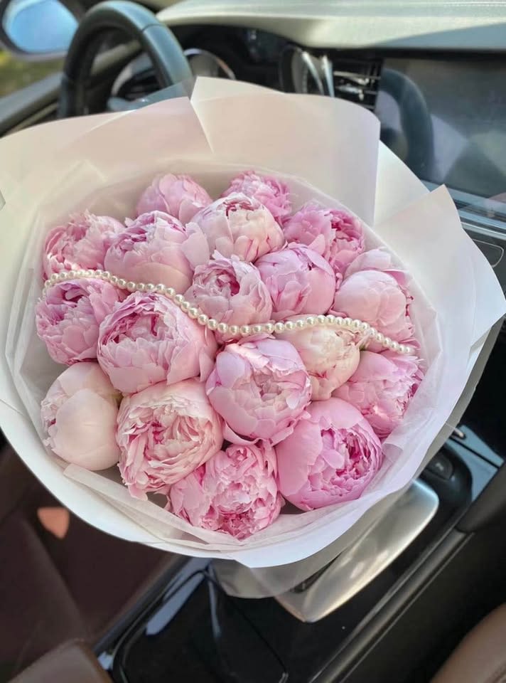 Pink peony bouquet wrapped in white paper with a pearl strand