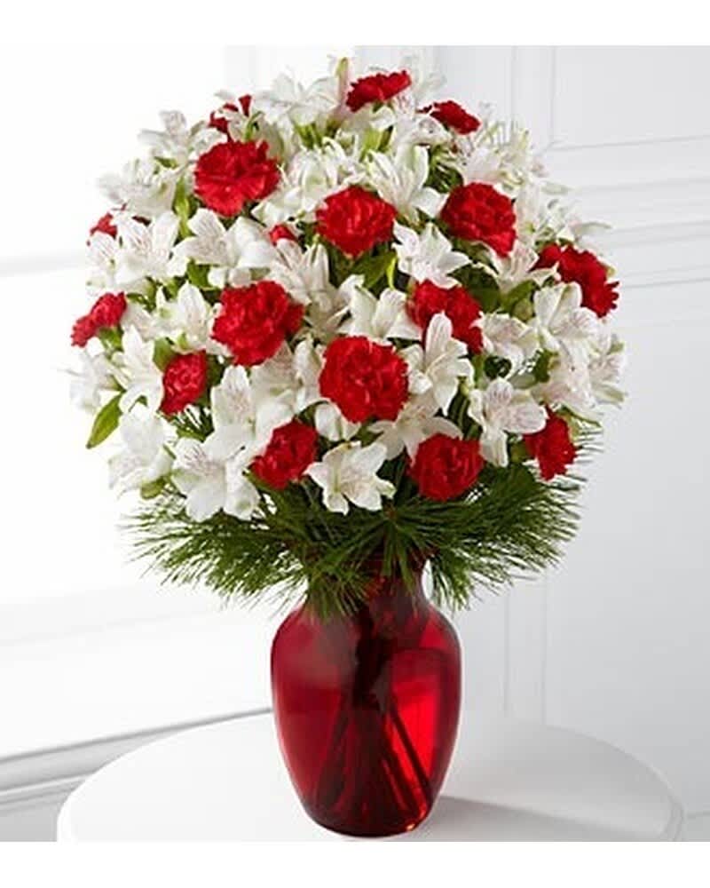 Red carnations and white alstroemeria arranged with pine in a red glass vase