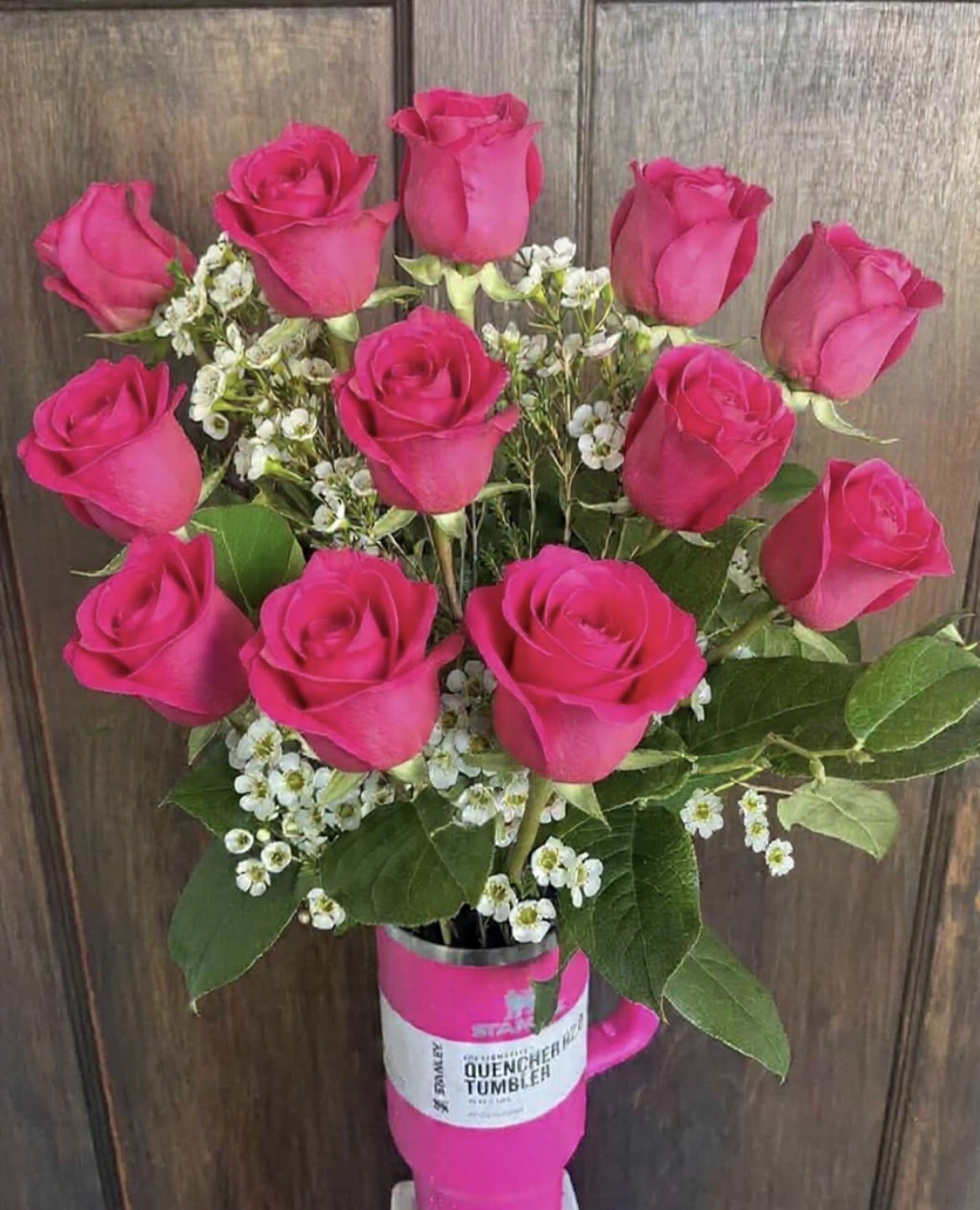 Hot pink roses arranged in a pink tumbler with small white filler flowers