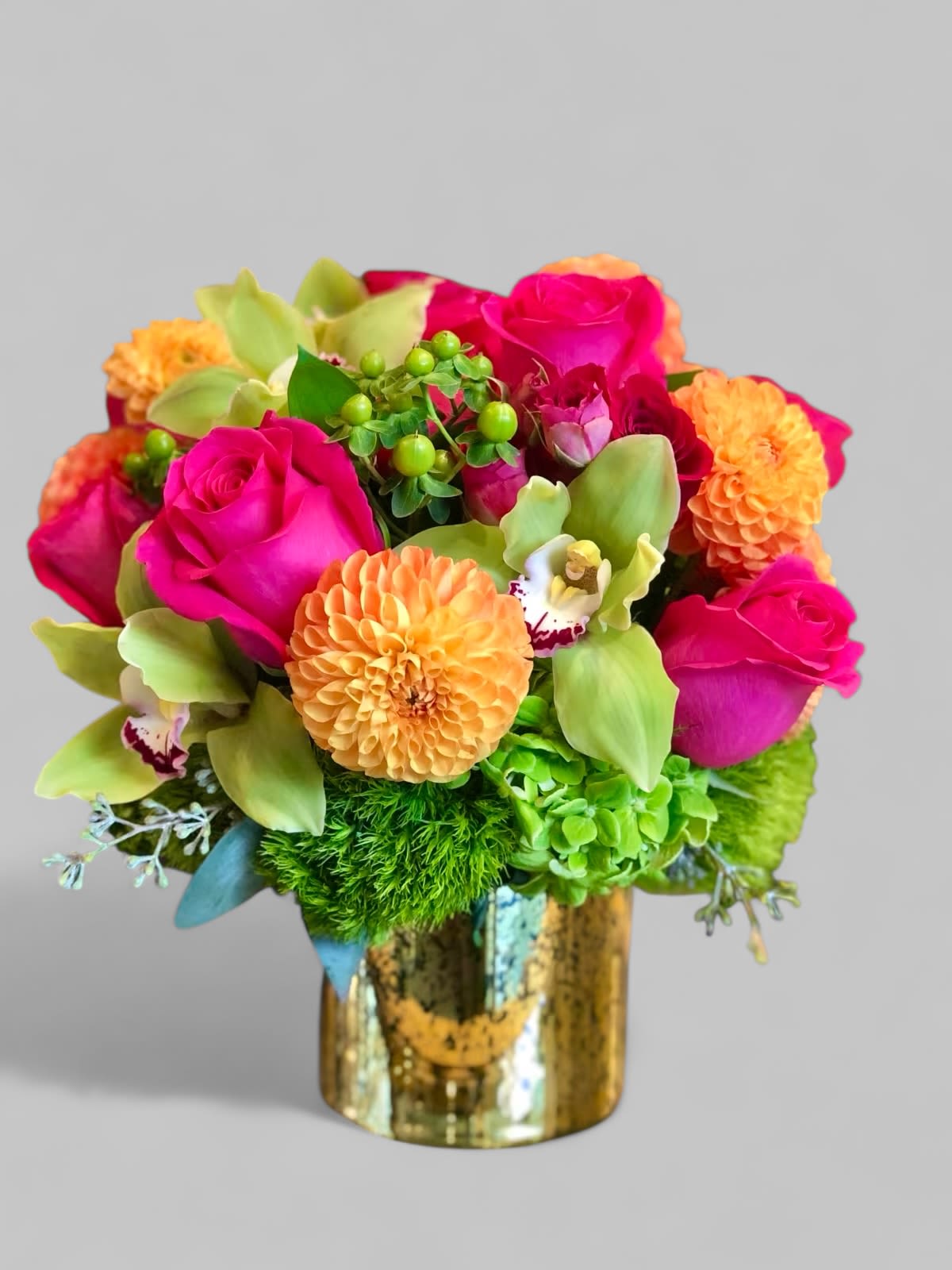 Orange Light  - A bright floral arrangement in a gold vase, with hot pink Roses, orange Dahlias, and green Cymbidium Orchids, with green Hydrangea and Dianthus. The perfect size arrangement for a desktop or a side table!