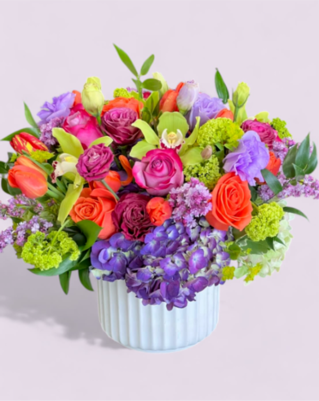 Bright mixed arrangement of orange, pink, and purple flowers in a white ceramic vase