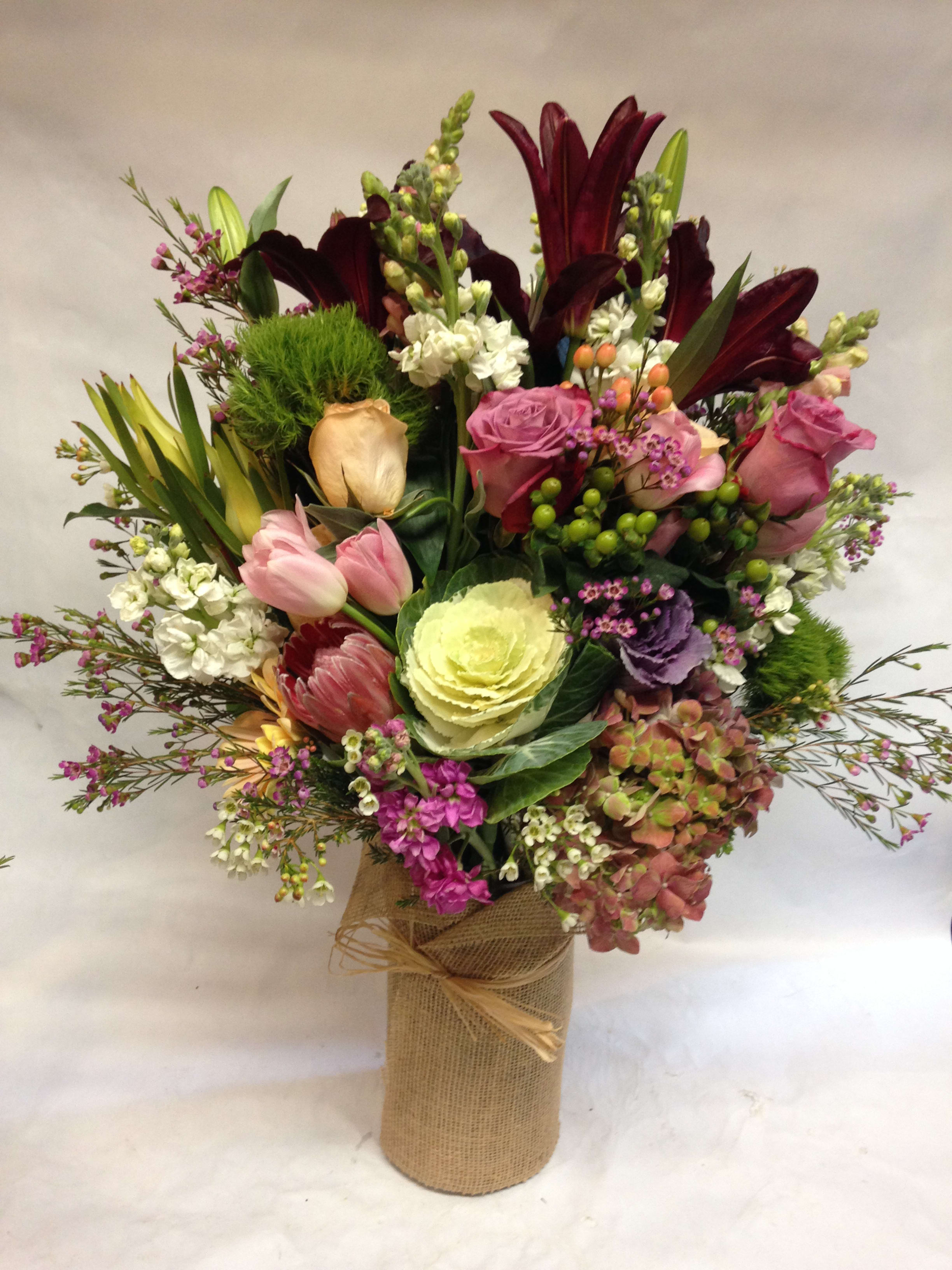 Mixed bouquet with lilies, roses, tulips, and hydrangea in a burlap-wrapped vase