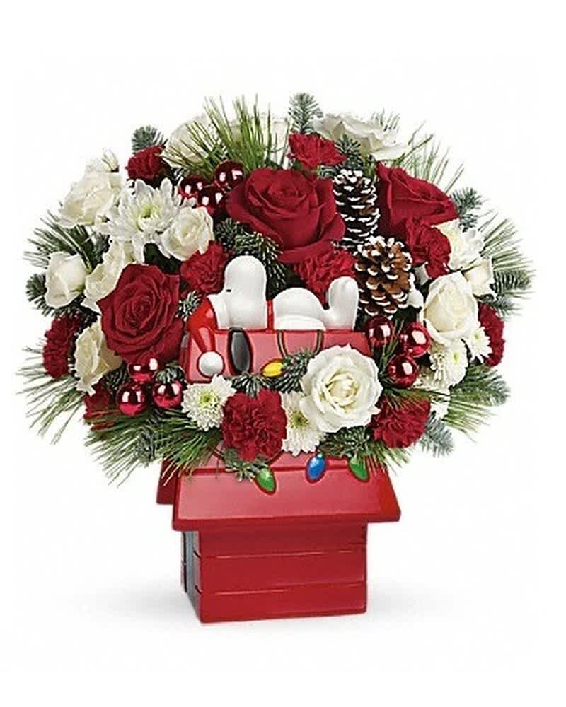 Red and white Christmas flower arrangement in a Snoopy doghouse container with pinecones and ornaments