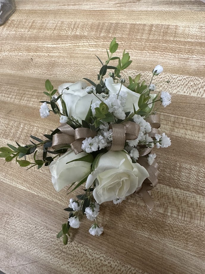  The Spray Rose Corsage Set - A delicate white rose corsage and matching boutonniere set that reads as timeless and romantic-perfect for prom, weddings, or any formal celebration where refined elegance matters. The compact corsage and boutonniere communicate thoughtfulness: the white roses and tiny white filler flowers create a soft, classic look that makes the wearer feel cherished and polished.  Each corsage is finished with a soft satin ribbon and a comfortable wristlet band, while the boutonniere is wrapped to match and secured with a boutonniere pin for easy wear. Variations shown include alternatives with taupe or black ribbon, gold loops and decorative mesh for a brighter, gift-like effect, and clear plastic wrap for presentation-ready delivery. We can customize ribbon color to coordinate with your dress or event-wristlet and pin are included with the set for a complete, ready-to-wear look.