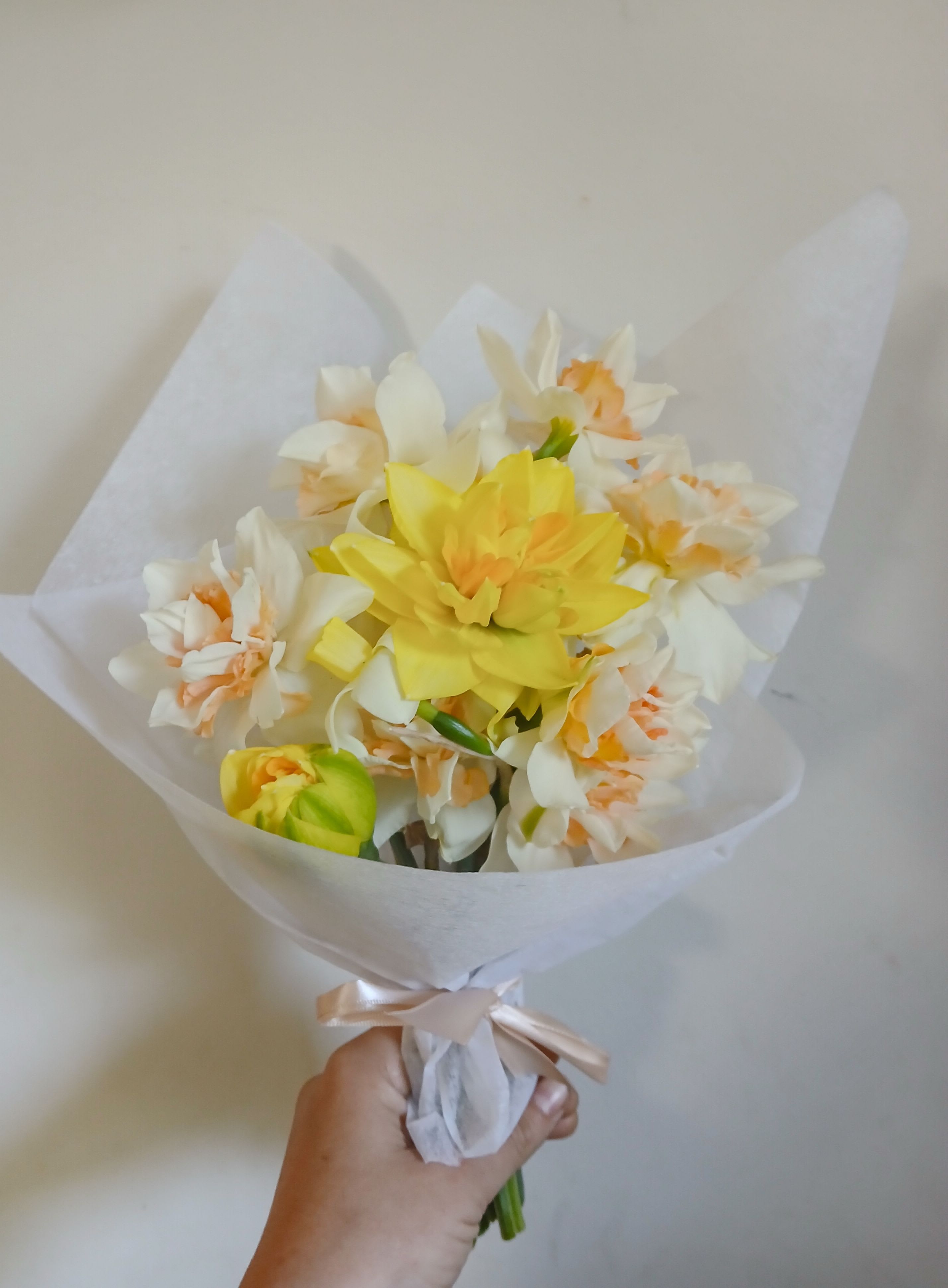 Handheld bouquet of yellow and white flowers wrapped in white paper