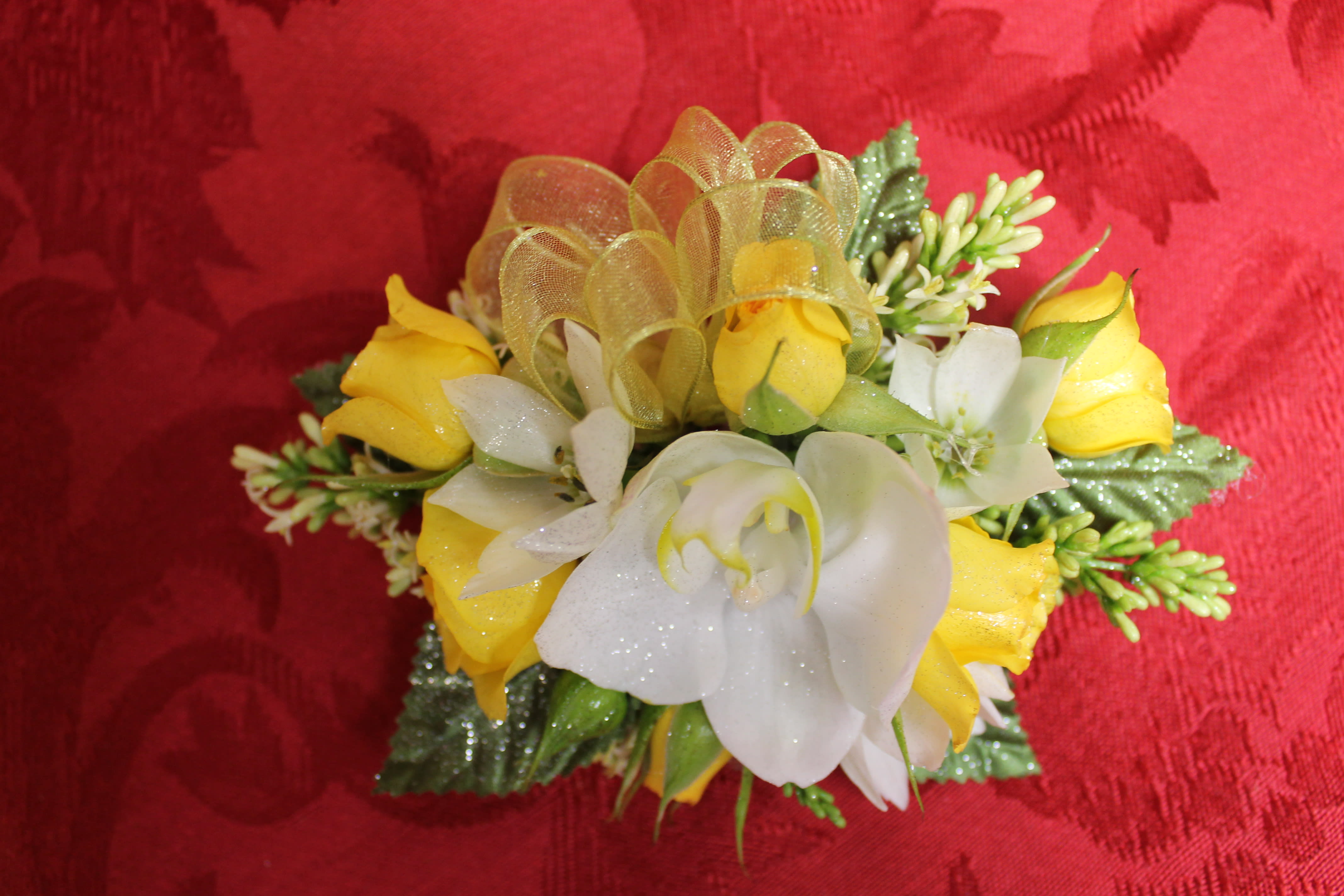 Small yellow and white floral corsage with ribbon on red fabric