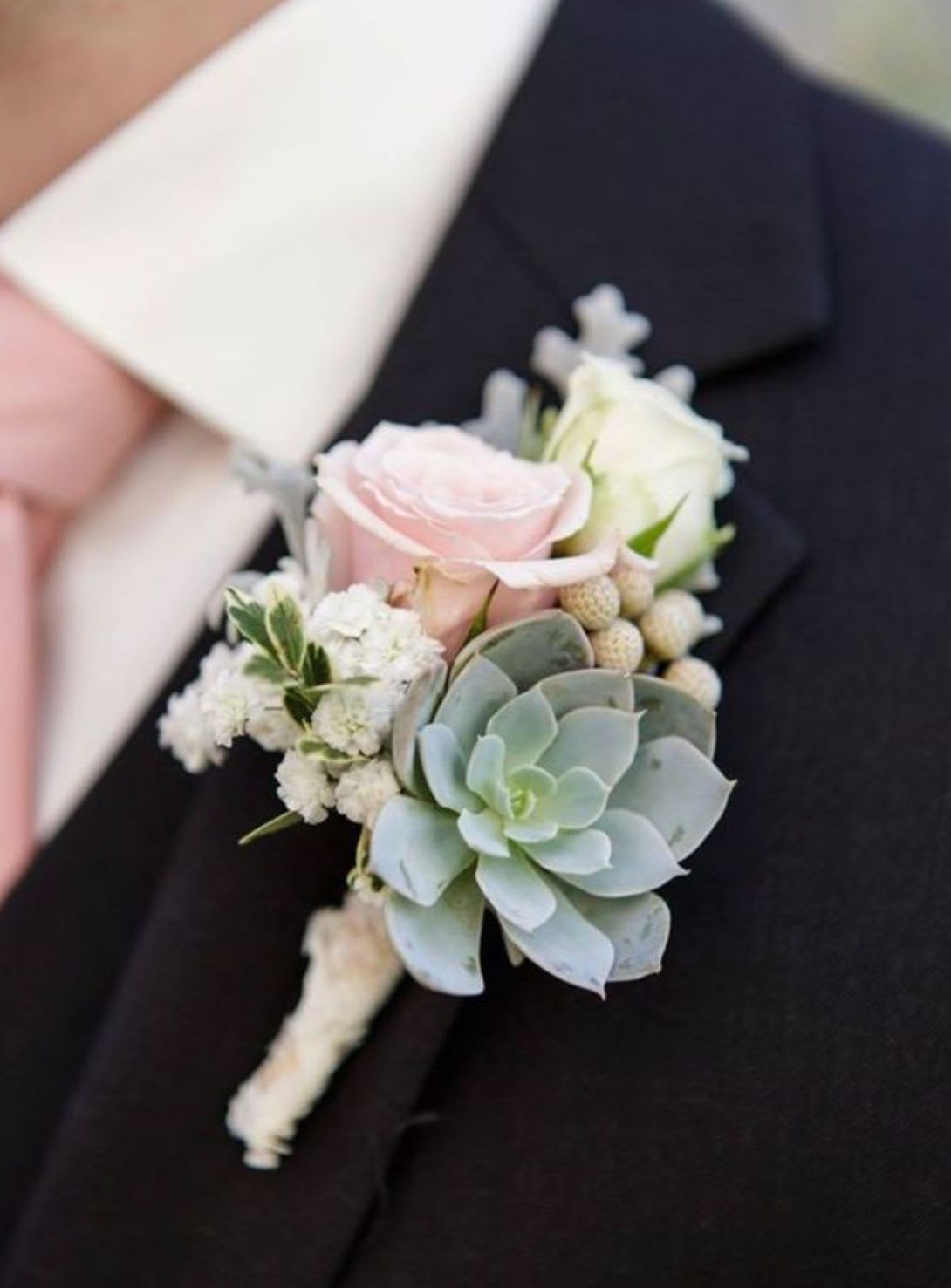 Boutonniere with pink and white roses and a succulent on a dark suit