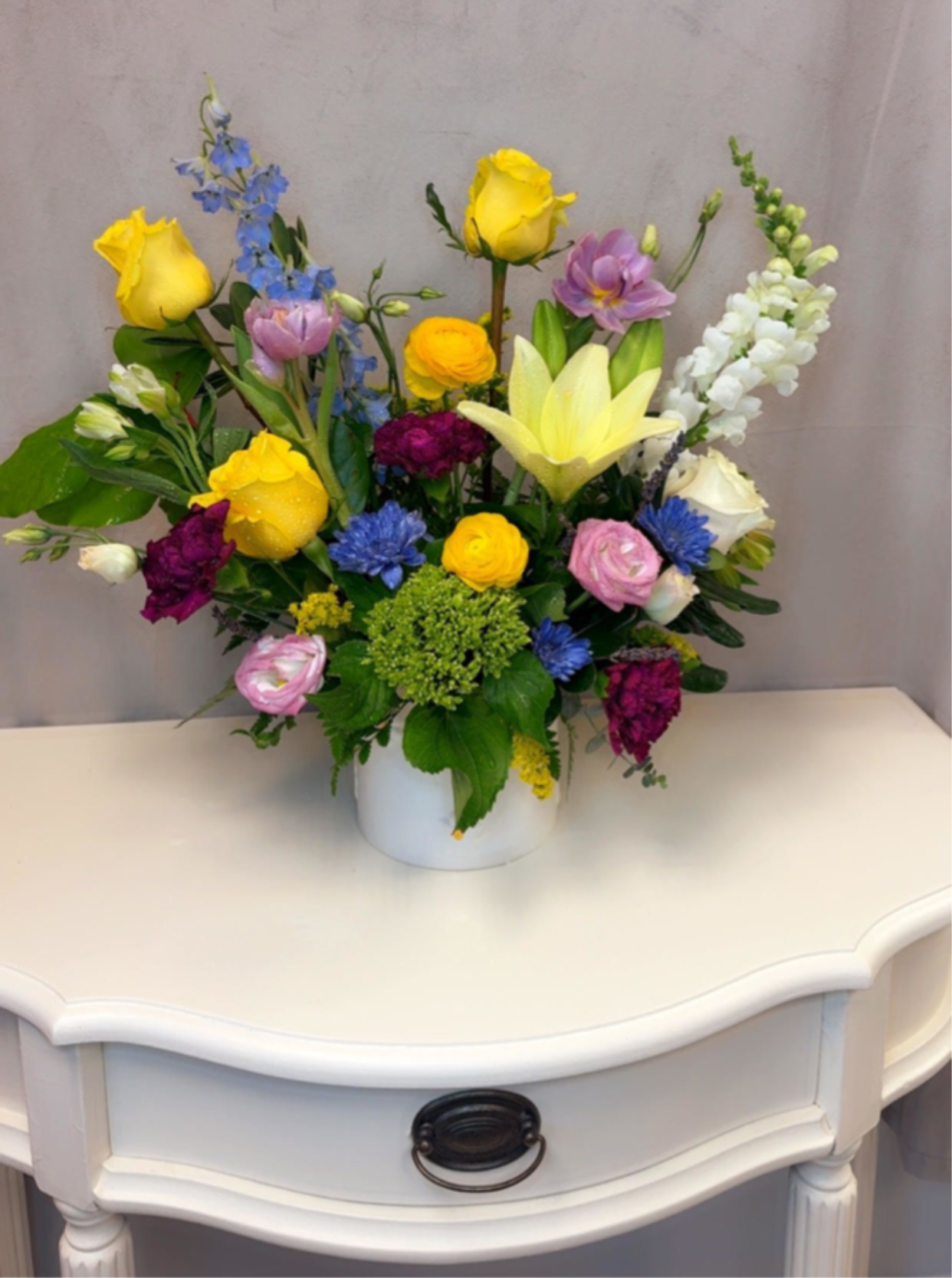 Golden Harmony - Golden Harmony is a vibrant and uplifting floral arrangement designed to bring warmth and joy to any space. Featuring radiant yellow roses and lilies paired with soft pinks, rich magentas, and touches of fresh blue, this design captures the beauty of a blooming garden in perfect balance.  A lush mix of premium seasonal flowers adds texture and movement, while the modern white vessel keeps the look clean and refined. Bright, cheerful, and full of life, Golden Harmony is perfect for birthdays, celebrations, thank-you gifts, or simply making someone smile.  Handcrafted with care, this arrangement is a beautiful expression of color, energy, and effortless elegance