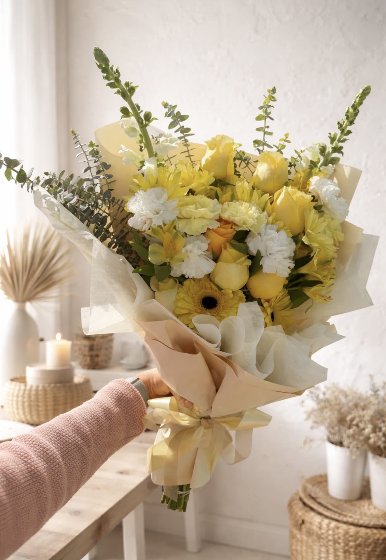 Blossom Joy Bouquet. - Sunlit yellow roses and tall snapdragon spikes make a cheerful first impression in this hand-tied flower arrangement-perfect as a birthday bouquet, a Mother's Day surprise, or a sunny "thinking of you" gift. The Blossom Joy Bouquet blends roses, gerbera-like daisy blooms, carnations, alstroemeria and vertical snapdragons to create a fresh, garden-style look that reads bright and airy for spring, summer, or any day someone needs a lift.  Creamy paper wrap and a pale ribbon soften the palette of yellow, white, green and peach while the mix of rounded blooms and vertical stems adds texture and movement. The loose, slightly rustic composition suits many occasions-from housewarming, graduation, and get-well wishes to anniversaries, thank-yous, sympathy, or just-because moments-giving the recipient a warm, sunny impression that feels both thoughtful and effortless.