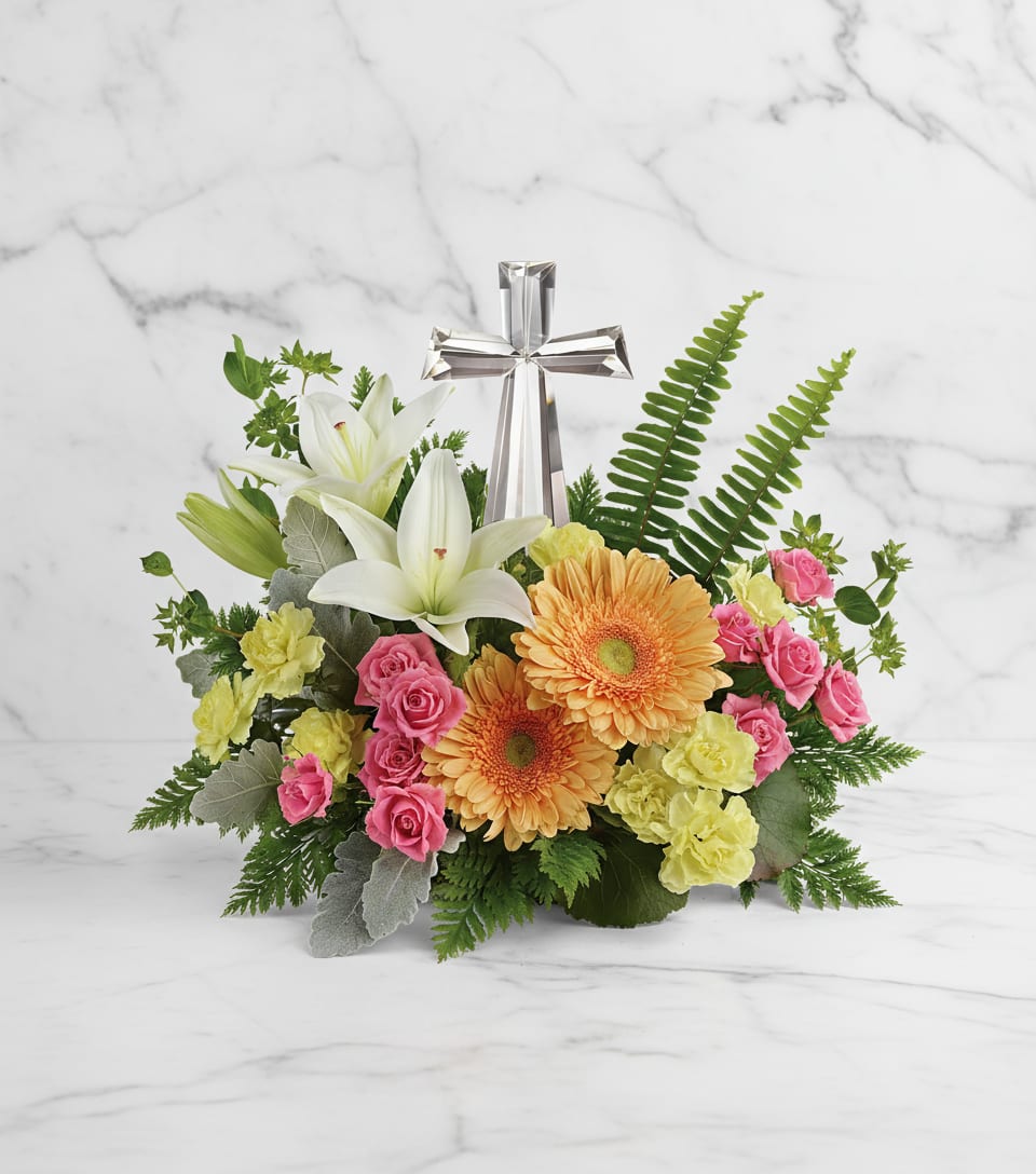 Floral arrangement with white lilies, pink roses, orange gerberas, and a silver cross