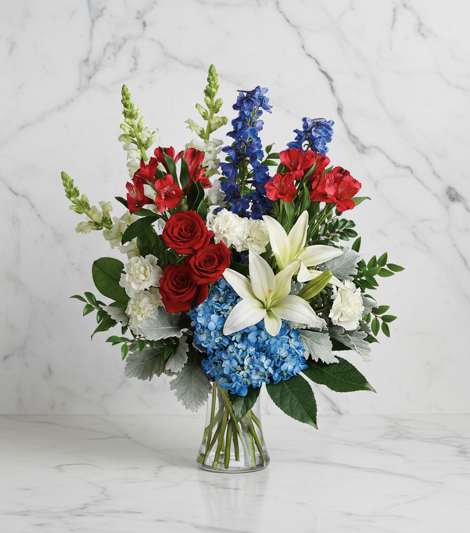 Colorful Tribute Bouquet - Perfectly patriotic with its red, white and blue blooms, this bold bouquet of hydrangea, lilies and roses is a versatile tribute on any occasion.  This bouquet features blue hydrangea, red roses, white asiatic lilies, red alstroemeria, white carnations, blue delphinium, white snapdragons, huckleberry, dusty miller, aralia leaf and lemon leaf. Delivered in a gathering vase  The scale of the arrangement should determine the type of substitution acceptable, but the substitution must be of equal or greater value and must maintain the style and color harmony of the original order.