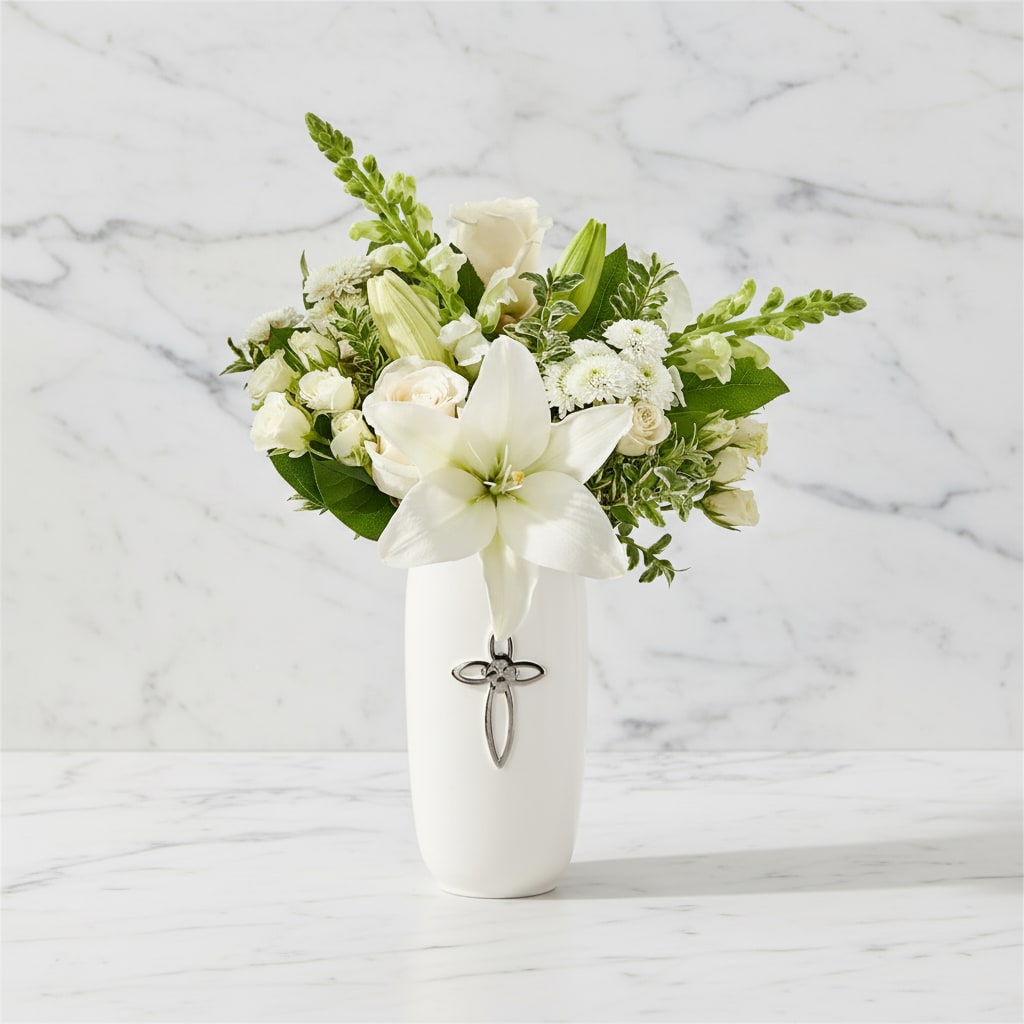 White lily and rose arrangement in a white vase with a cross charm