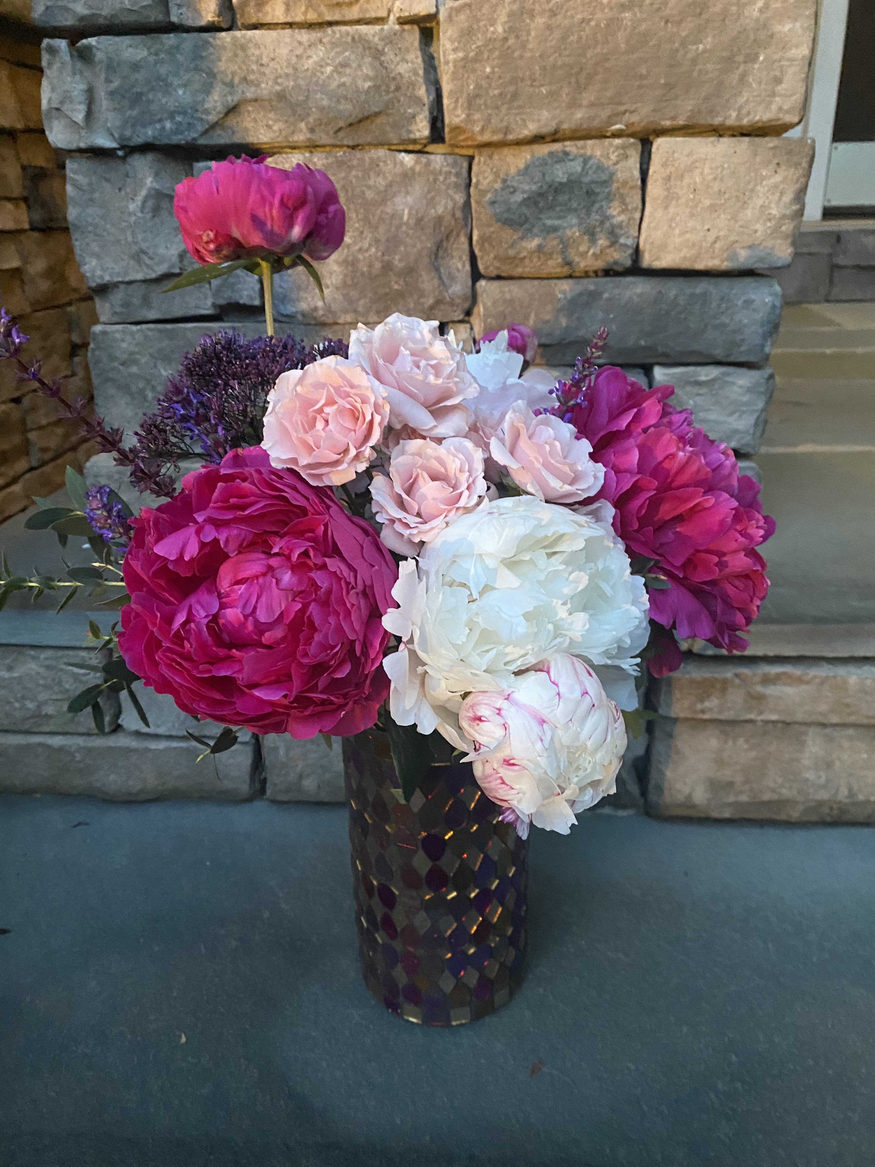 Pink and white peonies with small roses in a dark vase
