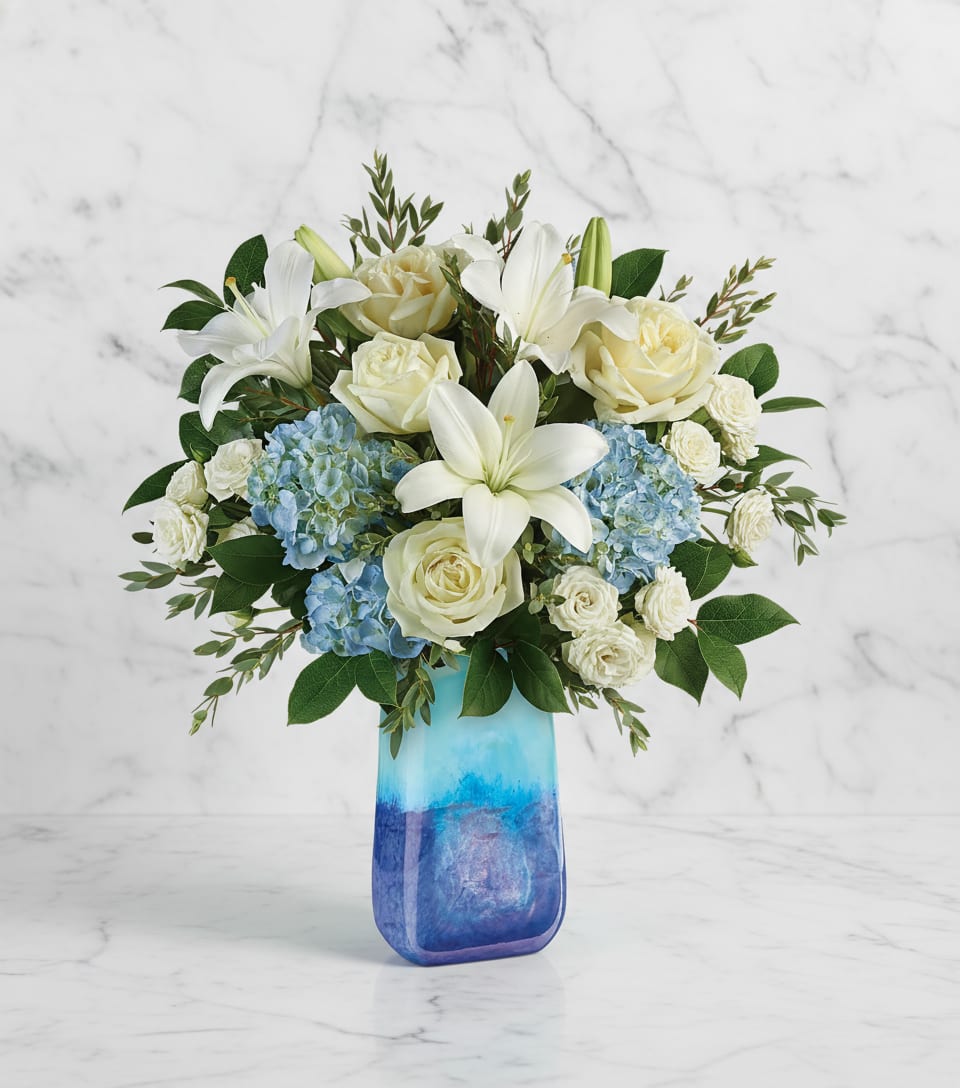 White lilies and roses with blue hydrangeas in a blue glass vase
