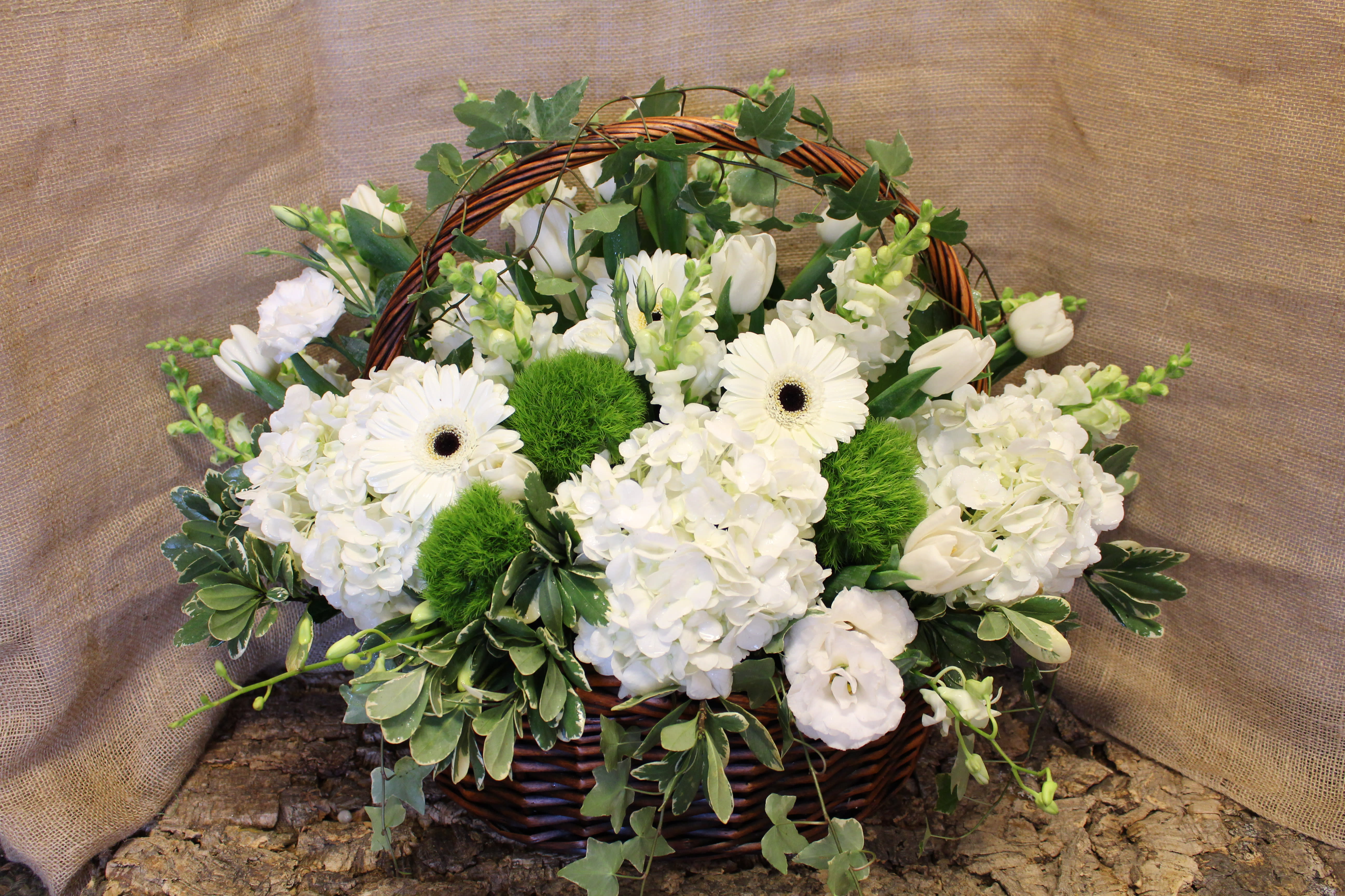 White flowers arranged in a wicker basket with green accents