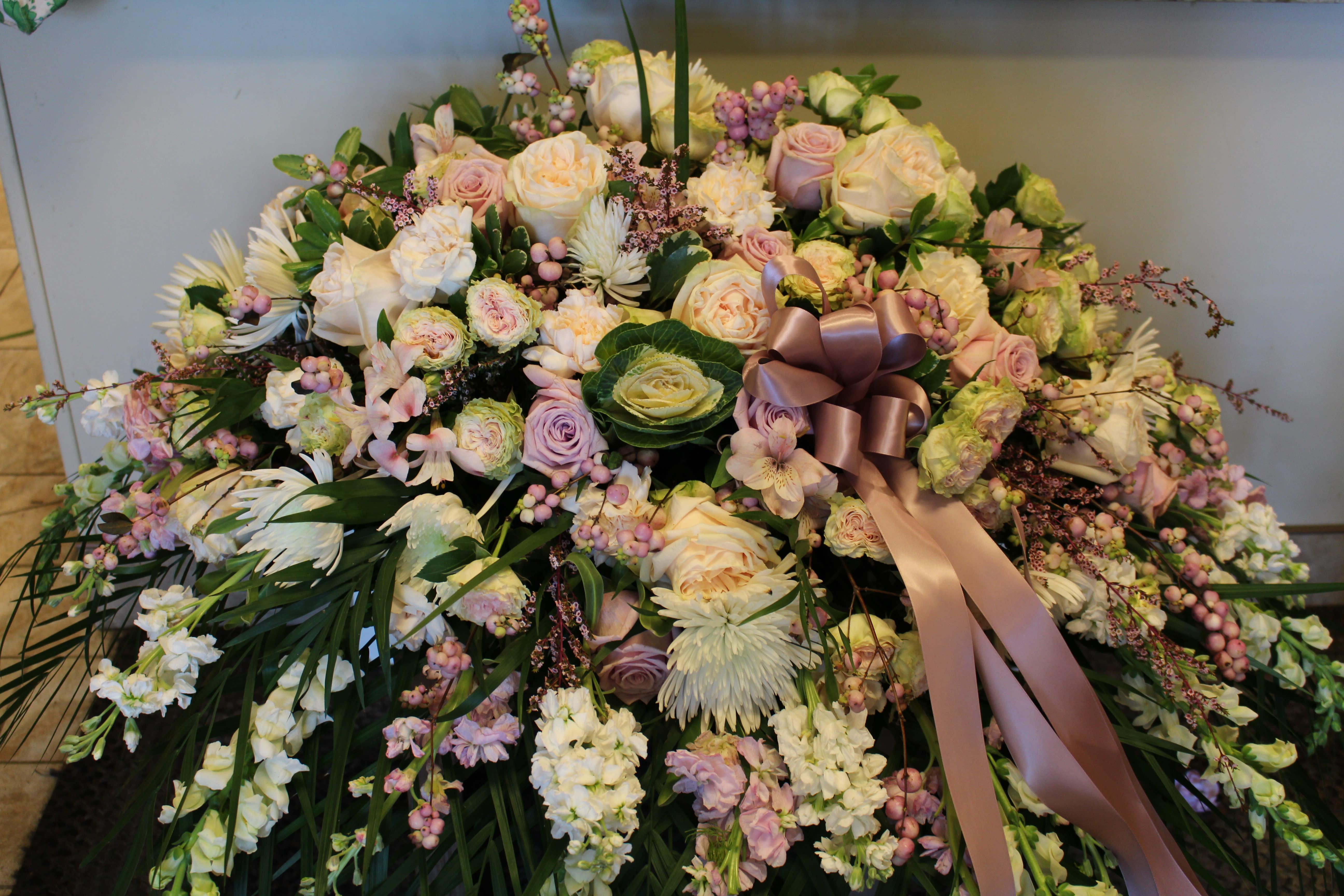 Large pastel floral arrangement with roses, daisies, and a satin ribbon