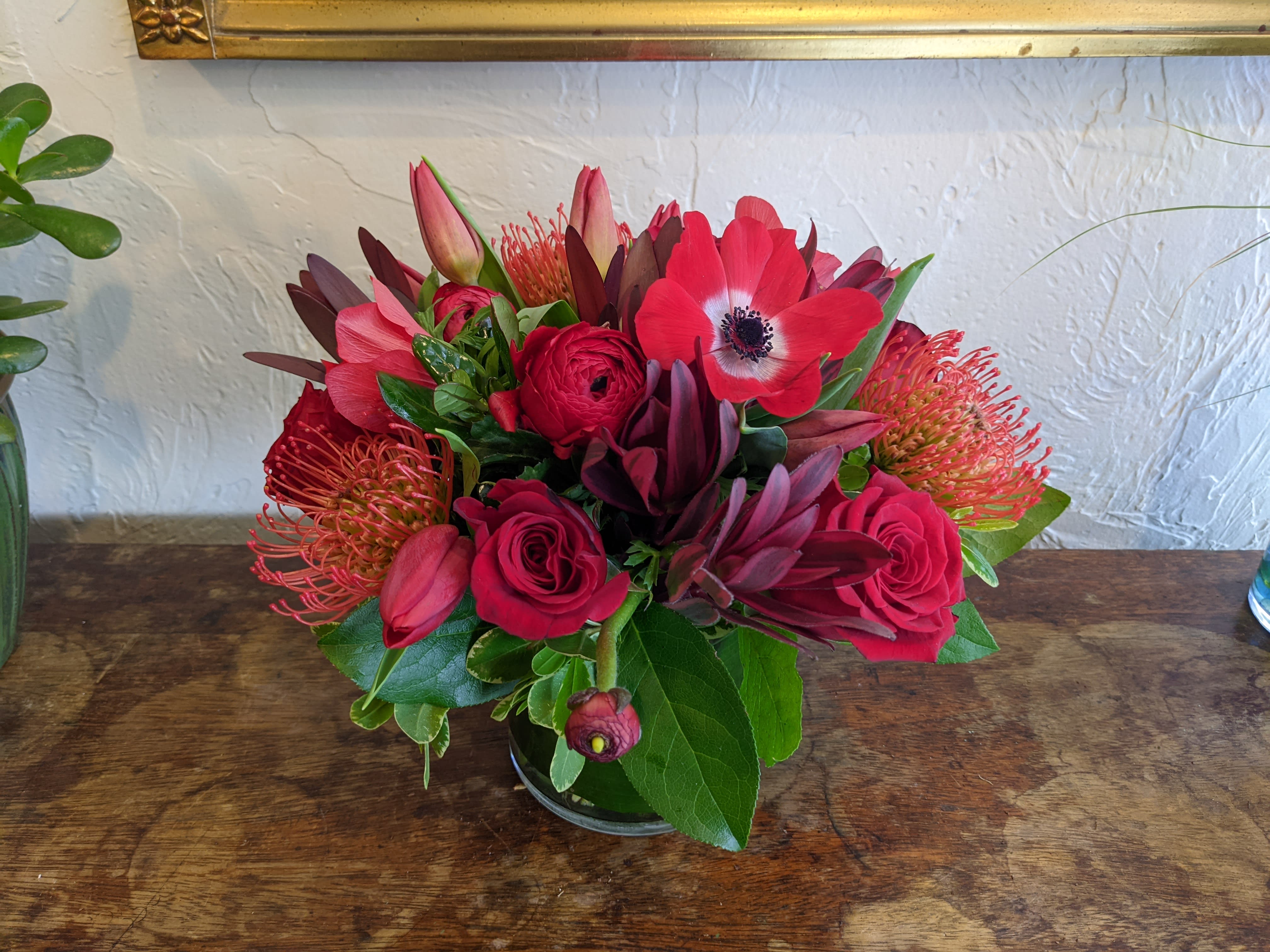 Monochrome Designer's Choice - Red - Pick the color and leave the flowers up to us with our Monochrome series Designer's Choice flower arrangements. These pieces feature a primary color pallet which we will design a beautiful arrangement of flowers around. Some accent colors may be used but the primary color scheme will designed with your chosen color in mind (Color listed in the name of this piece)    *Vase color and style may vary. Please note that the arrangement displayed in the picture is an example piece and flowers featured are not guaranteed to be replicated