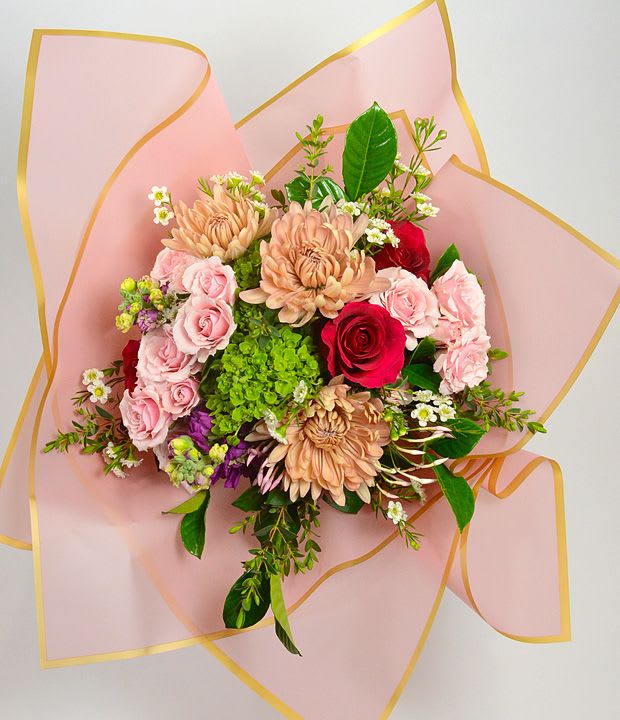 Bouquet of pink and red flowers wrapped in pale pink paper with gold trim