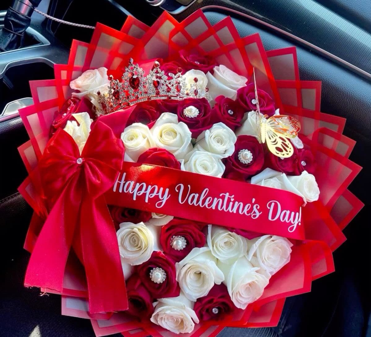 Round bouquet of red and white roses with a tiara and Happy Valentine’s Day ribbon.