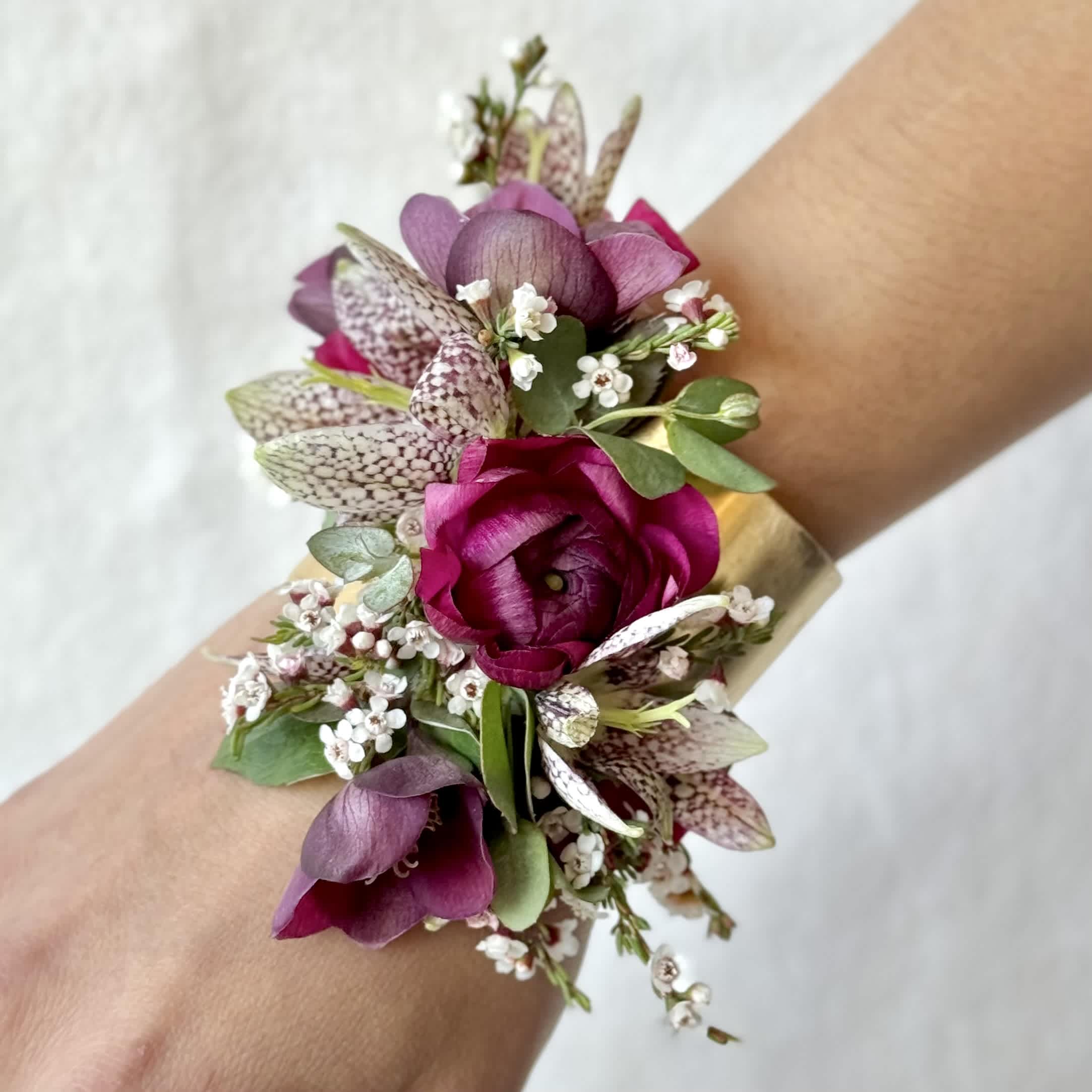 Purple floral wrist corsage with small white blossoms and green leaves
