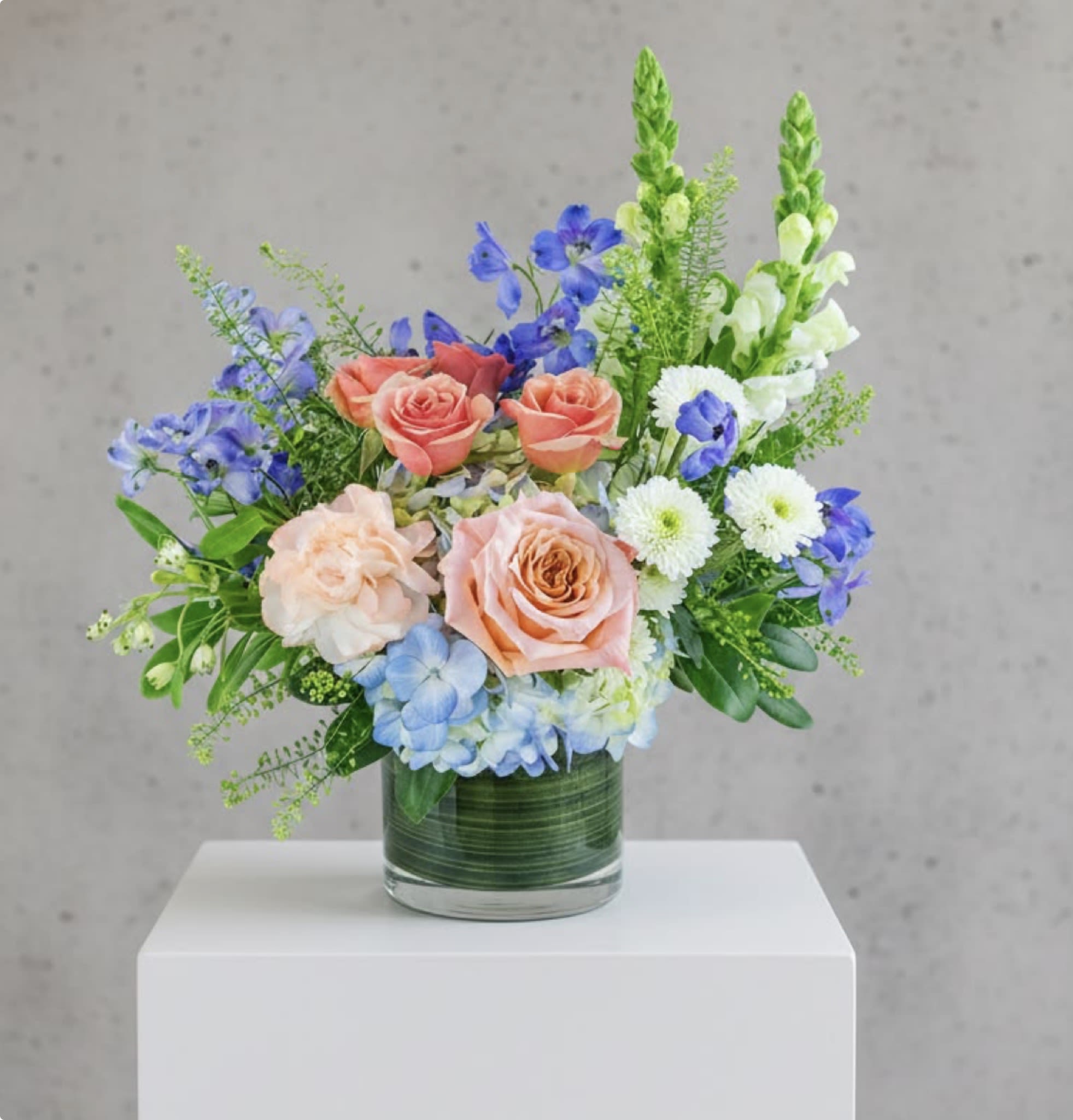 Mixed bouquet of roses, blue flowers, and white daisies in a glass vase