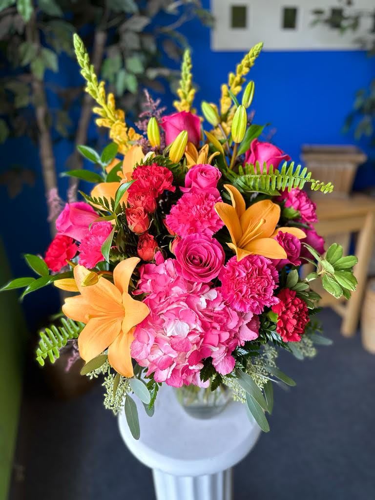 Bright pink and orange floral arrangement in a white vase