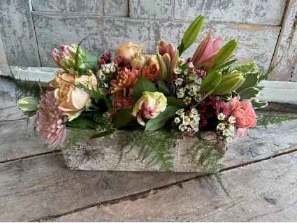 The Garden's Secret - This stunning centerpiece features seasonal blooms in soft peaches and pinks, presented in an earthy birchbark basket  Includes: Spray Roses, Parrot Tulips, Daisy Poms, Asiatic Lily, Wax Flower, Carnations, Chrysanthemum.